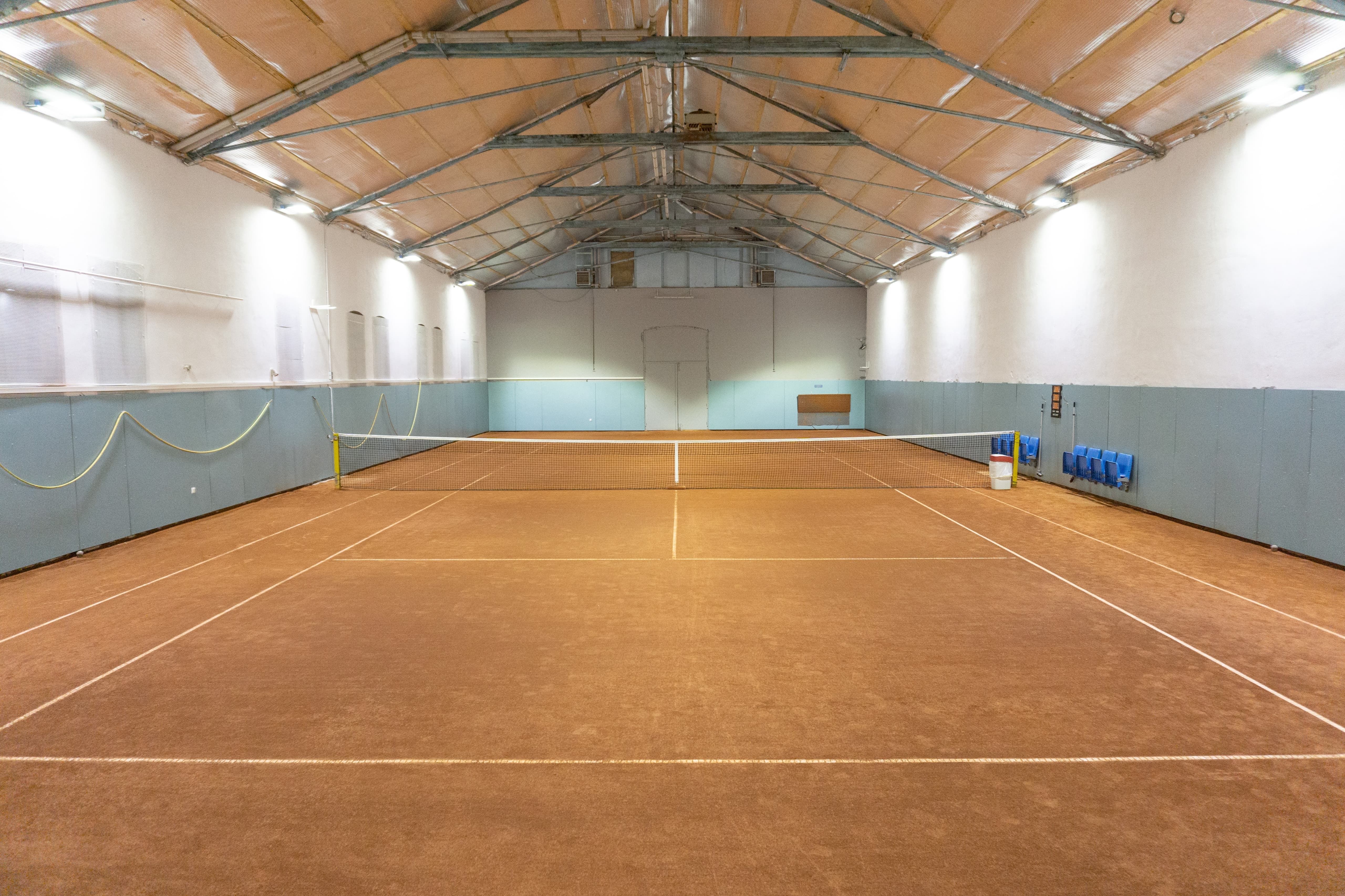 Interior view of an empty tennis court in a hall with a brown floor covering and blue walls.