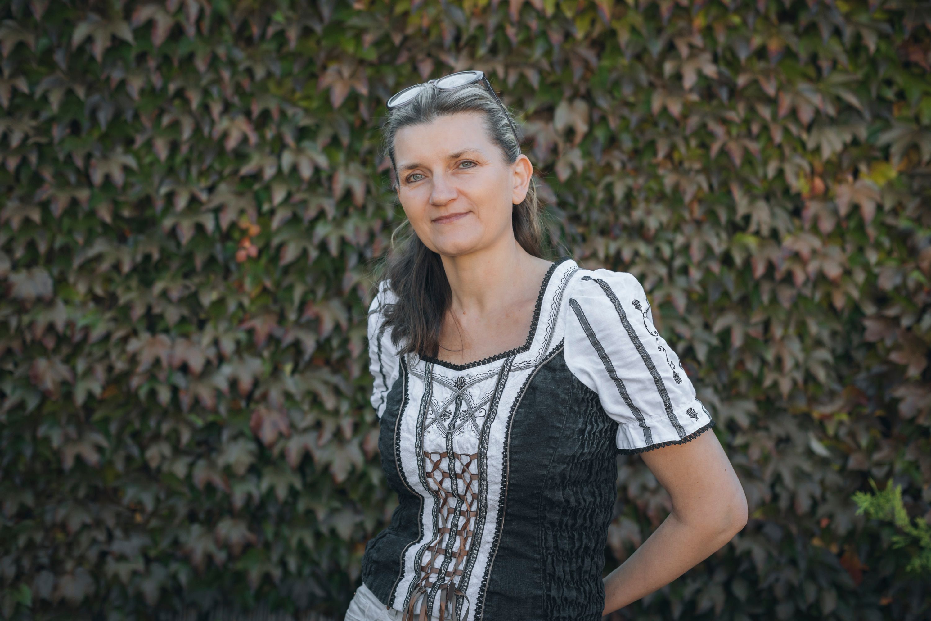 Woman in traditional dress in front of a wall overgrown with ivy.