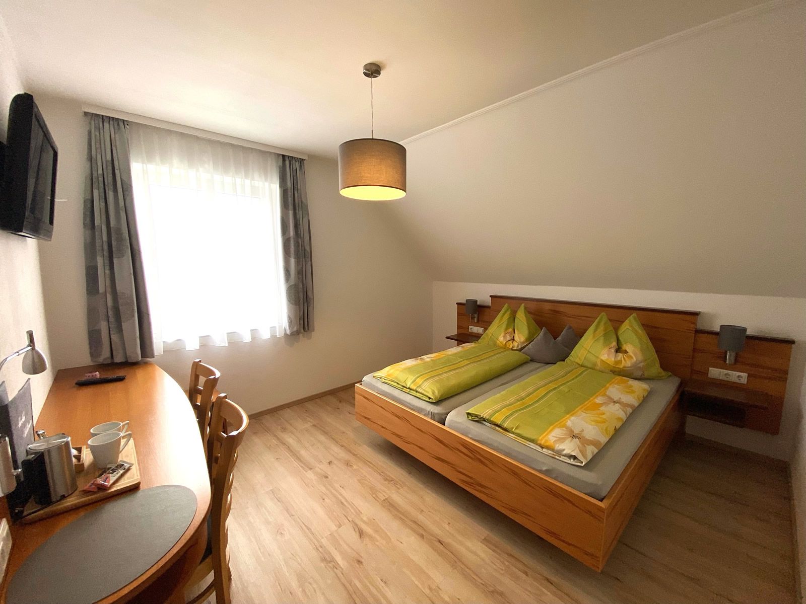 A cozy double room with a double bed, desk, chairs and a TV on the wall.