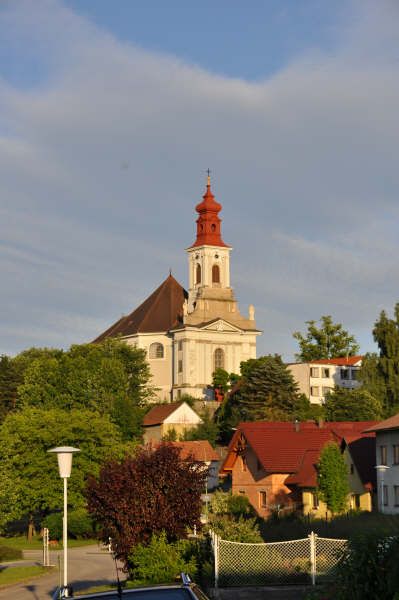 Pilgrimage church on a hill with red roofs and trees in the foreground.