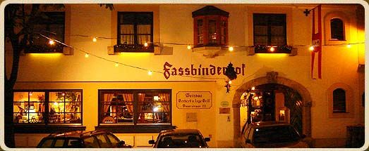 Night shot of a building with the inscription 'Fassbinderhof', illuminated by fairy lights.