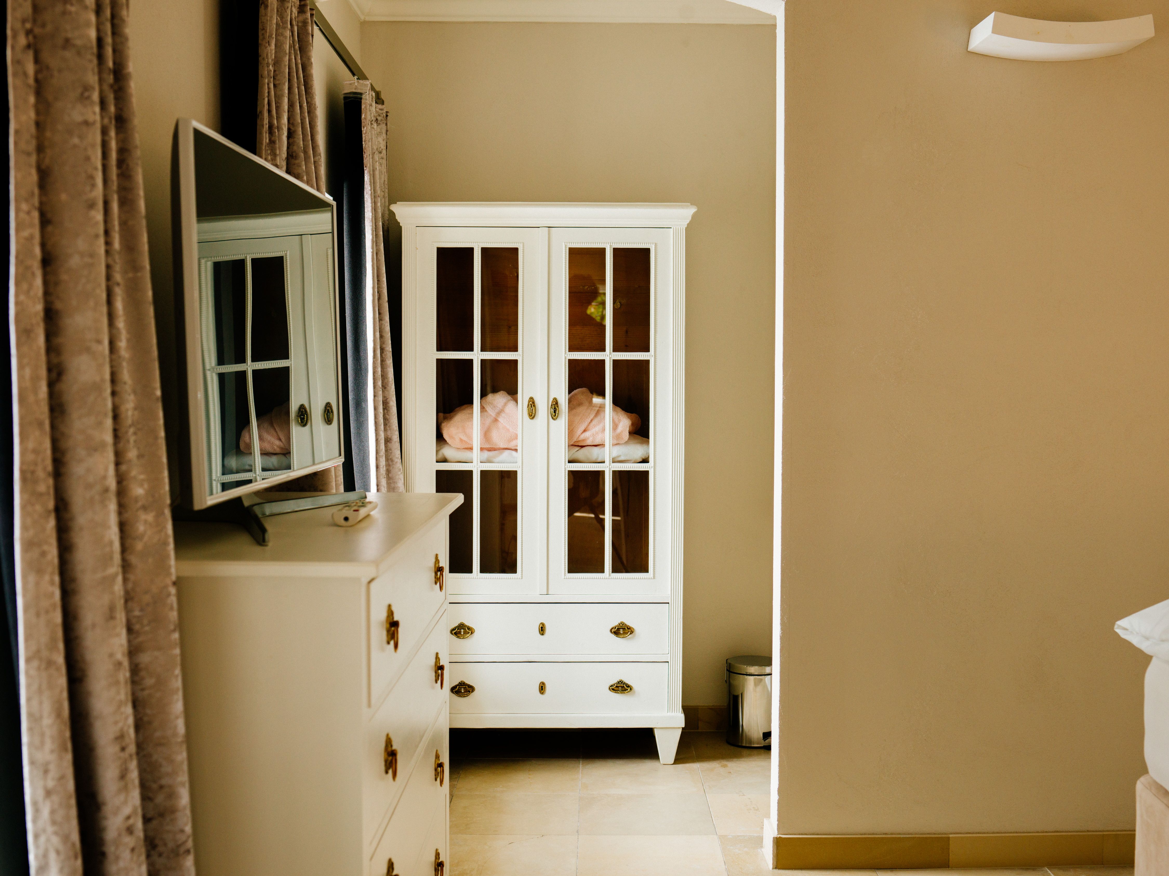 Interior view of a room with white wardrobe and chest of drawers, mirror and curtains.