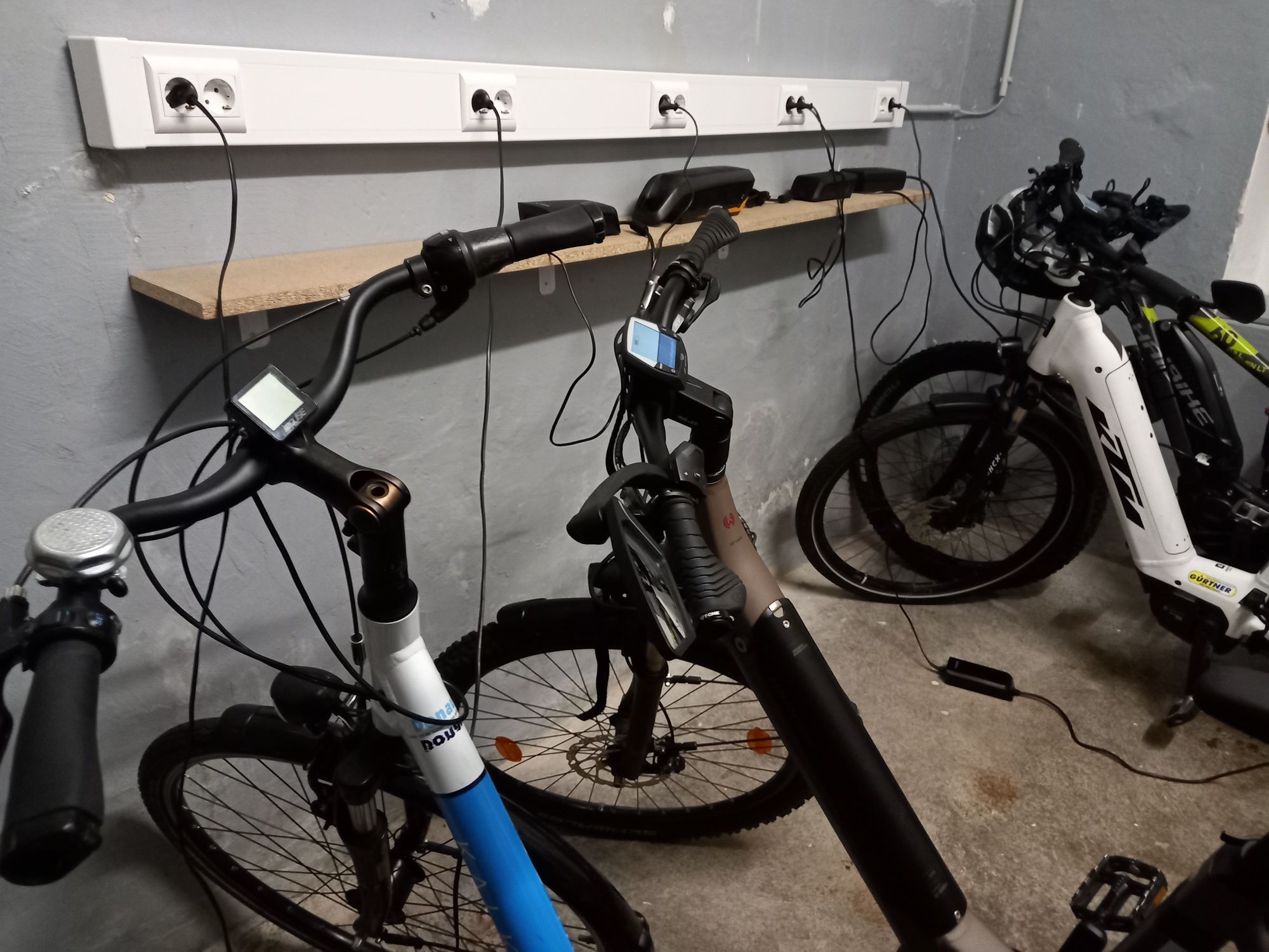 Three e-bikes in a garage being charged at a power strip.