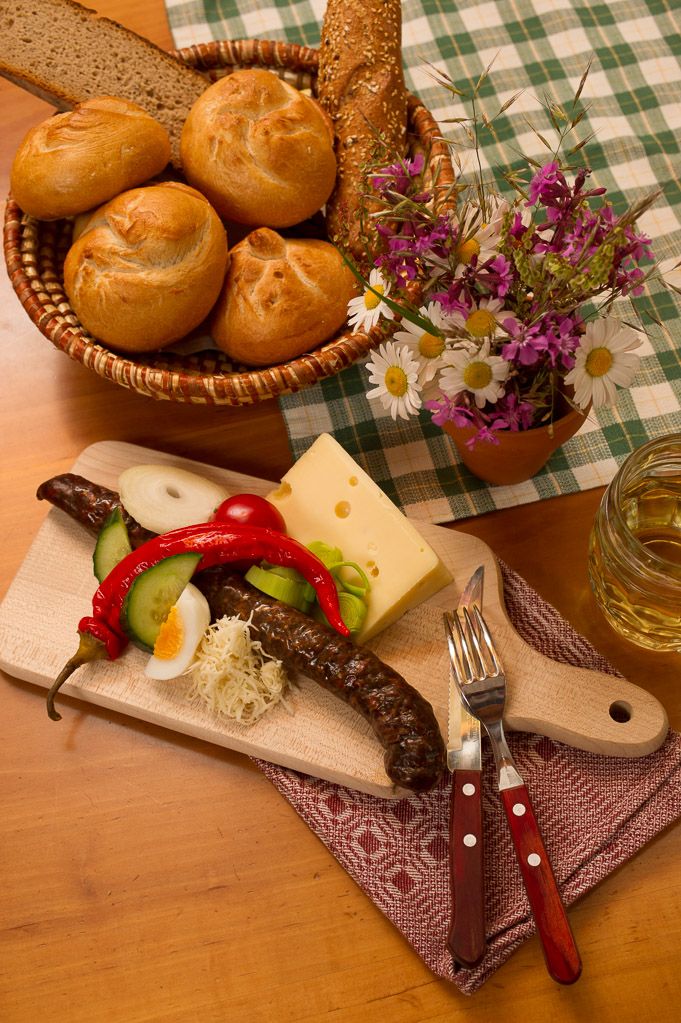 A traditional snack board with sausage, cheese, vegetables and bread on a wooden table.