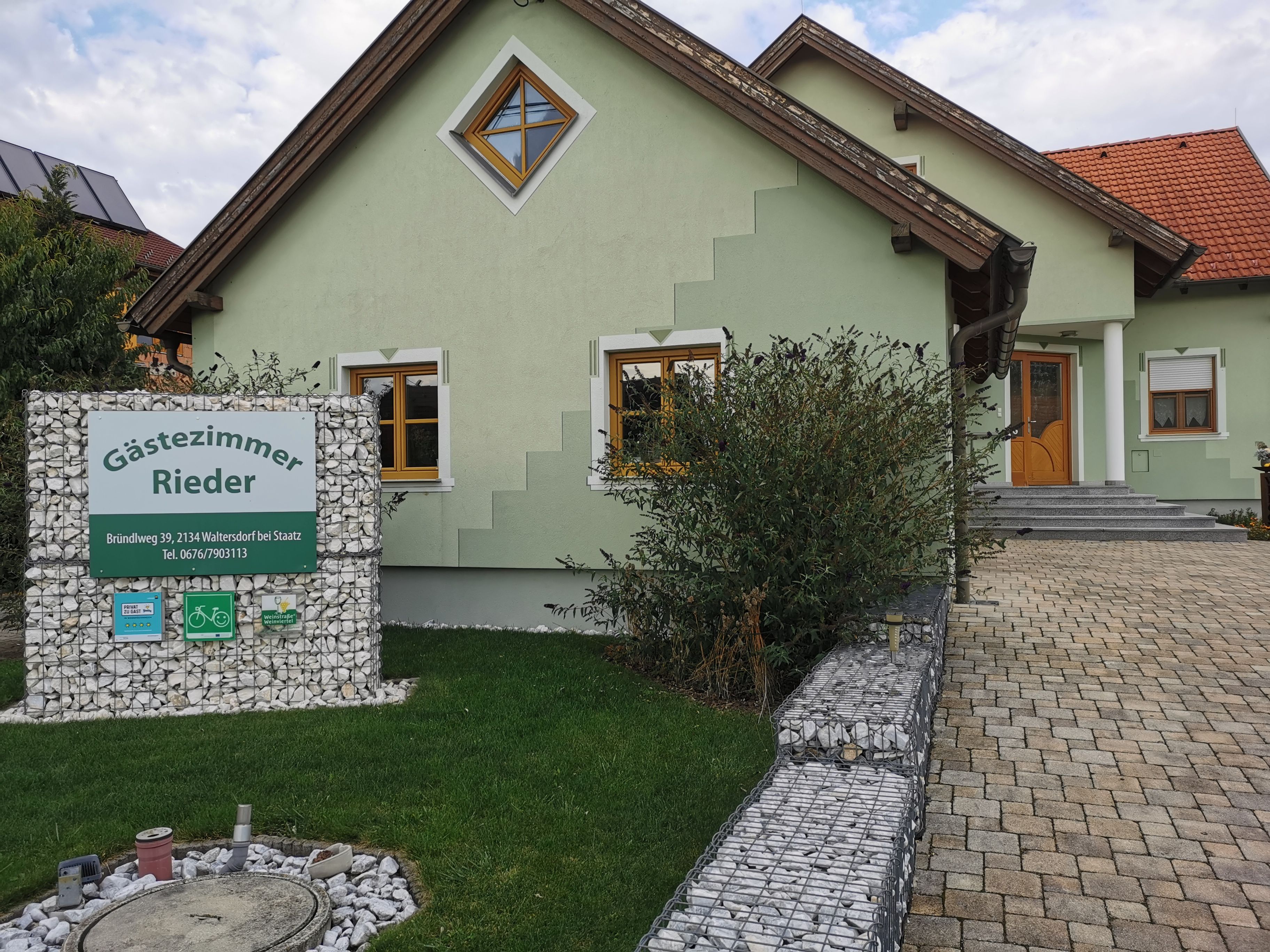 Green house with 'Gästezimmer Rieder' sign in the front garden.