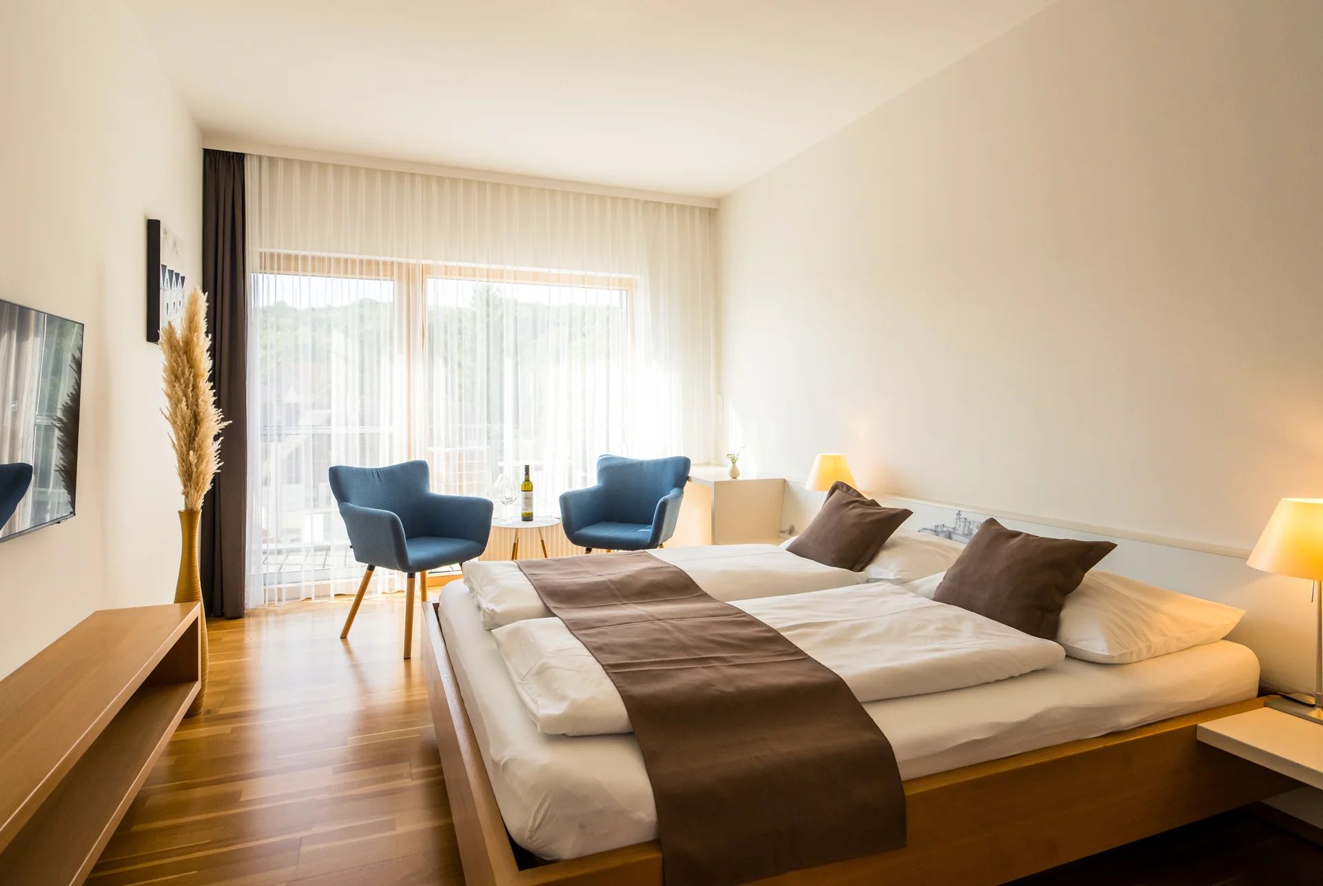 Modern guest room with double bed, blue armchairs and wooden floor.