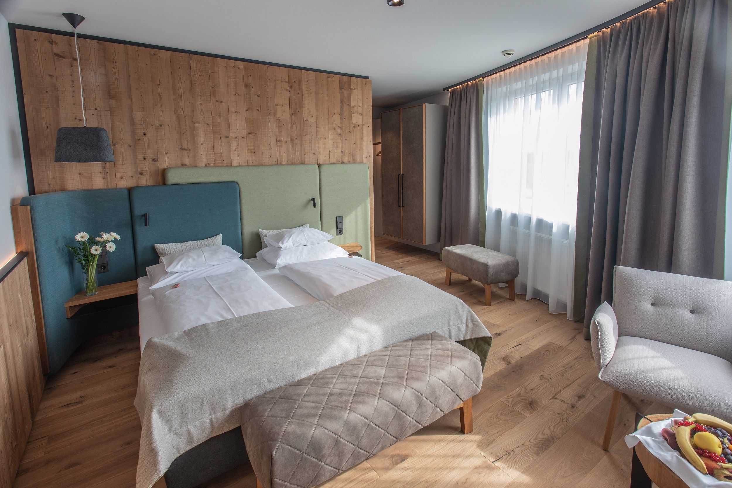 Modern hotel room with double bed, wooden walls and large windows.