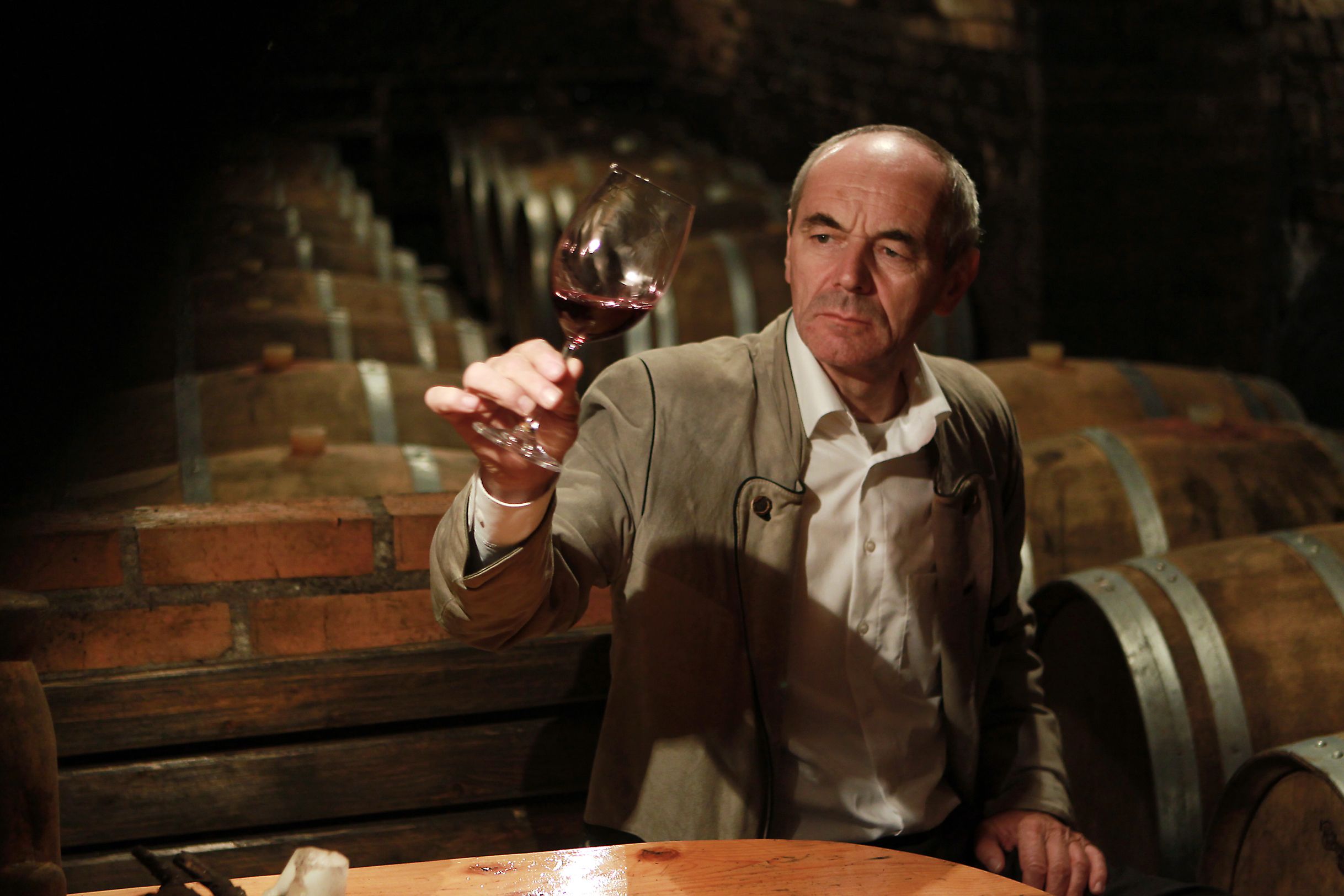 A man in the wine cellar holds up a glass of red wine.