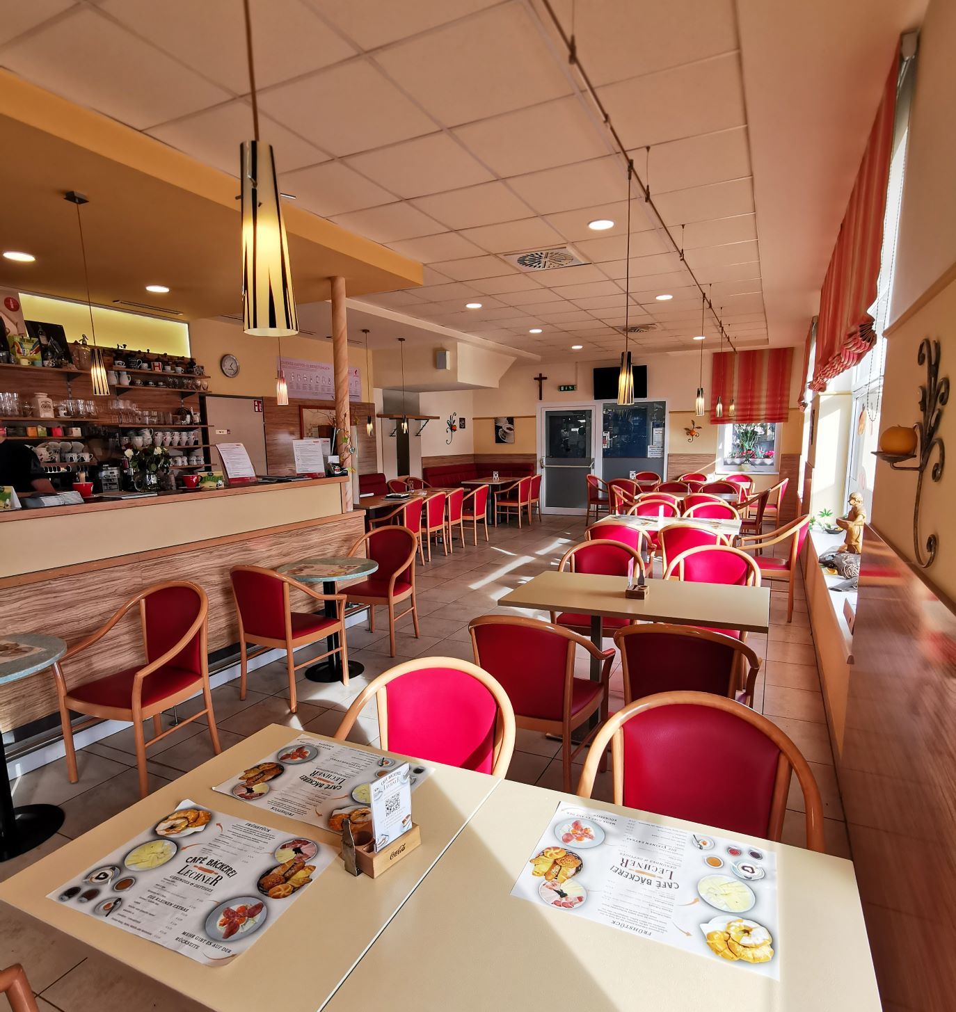 Interior view of a café with red chairs and tables, bar area on the left.
