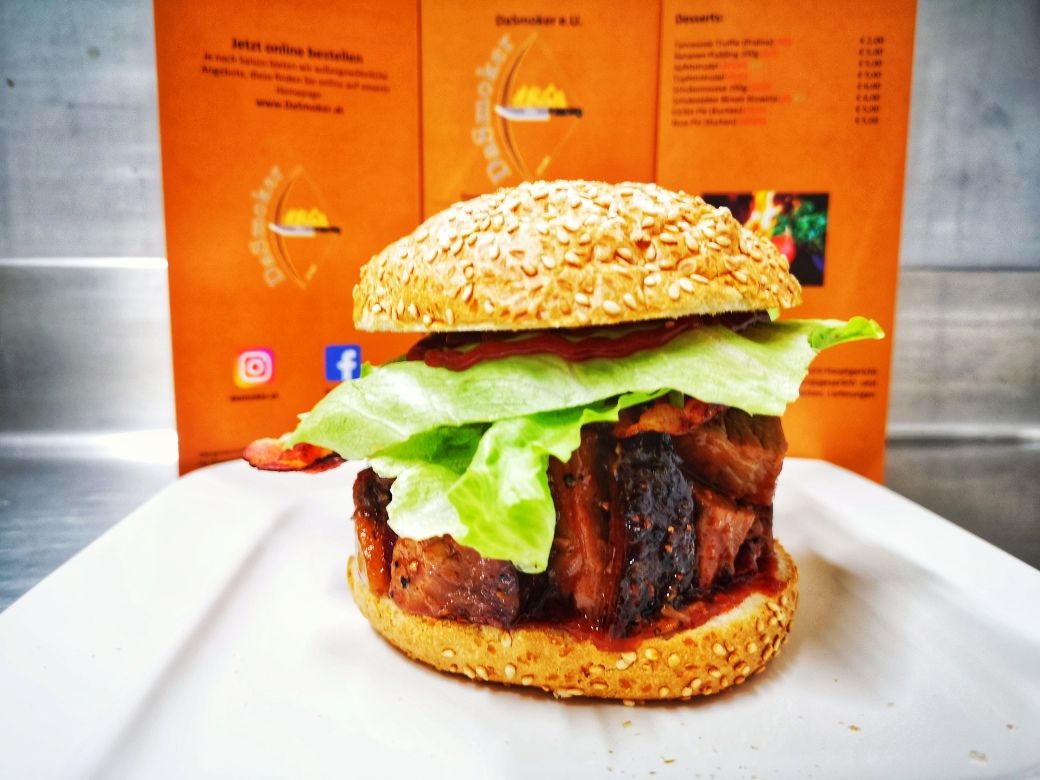 A burger with salad and meat on a white plate in front of an orange-colored menu.