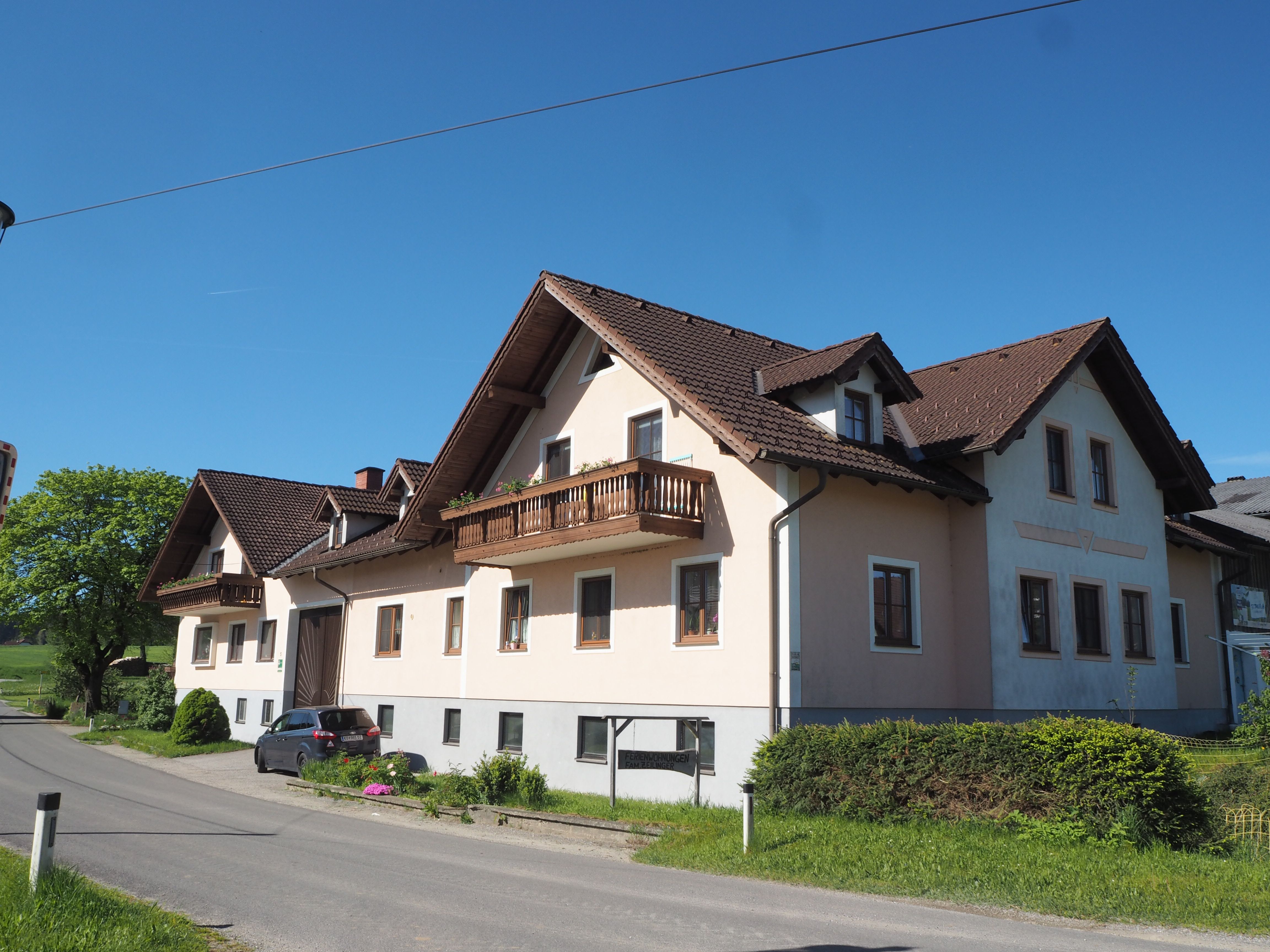 A large farmhouse with a brown roof and balconies on a country road under a clear sky.