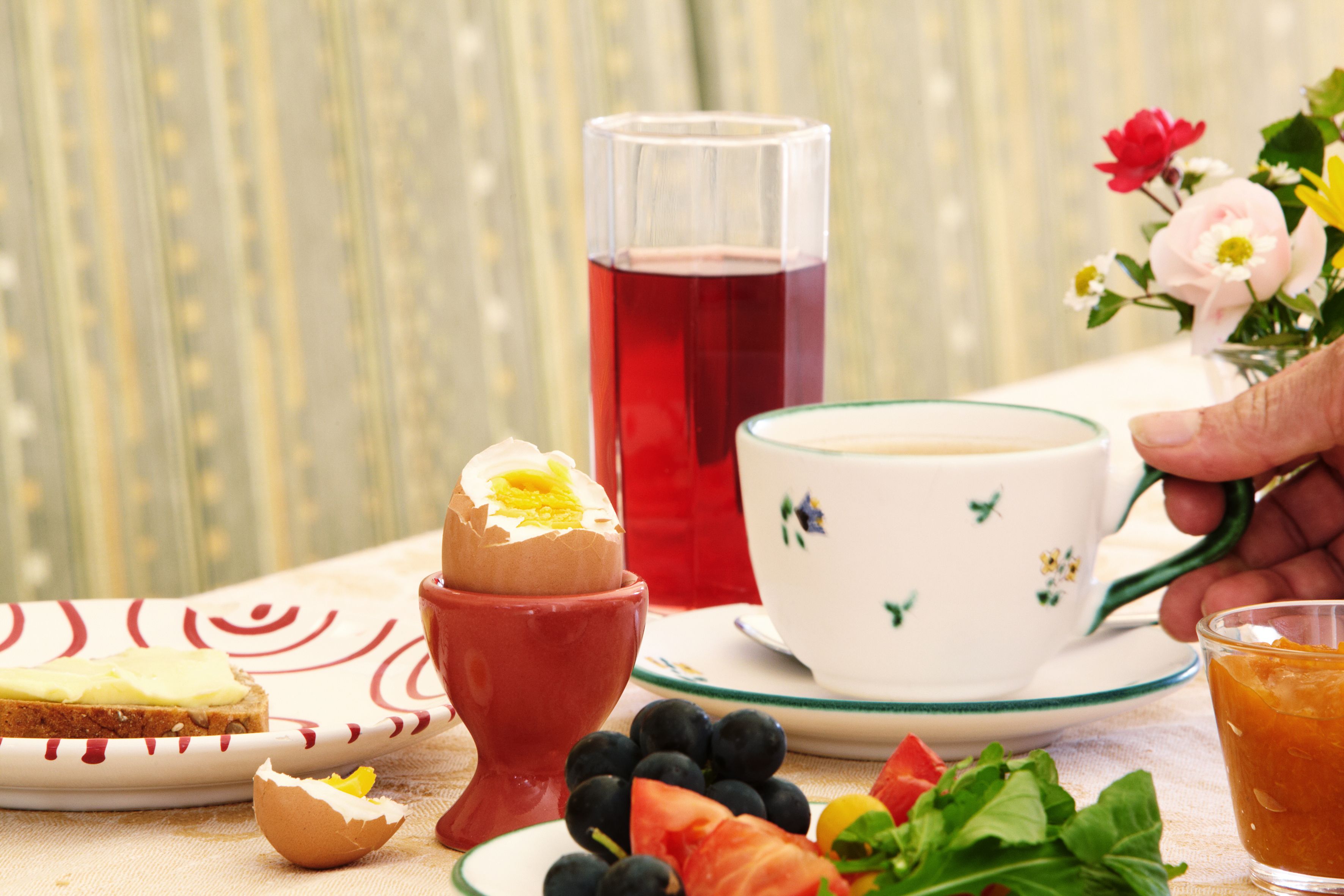 Breakfast table with boiled egg, juice, coffee, bread, fruit and flowers.
