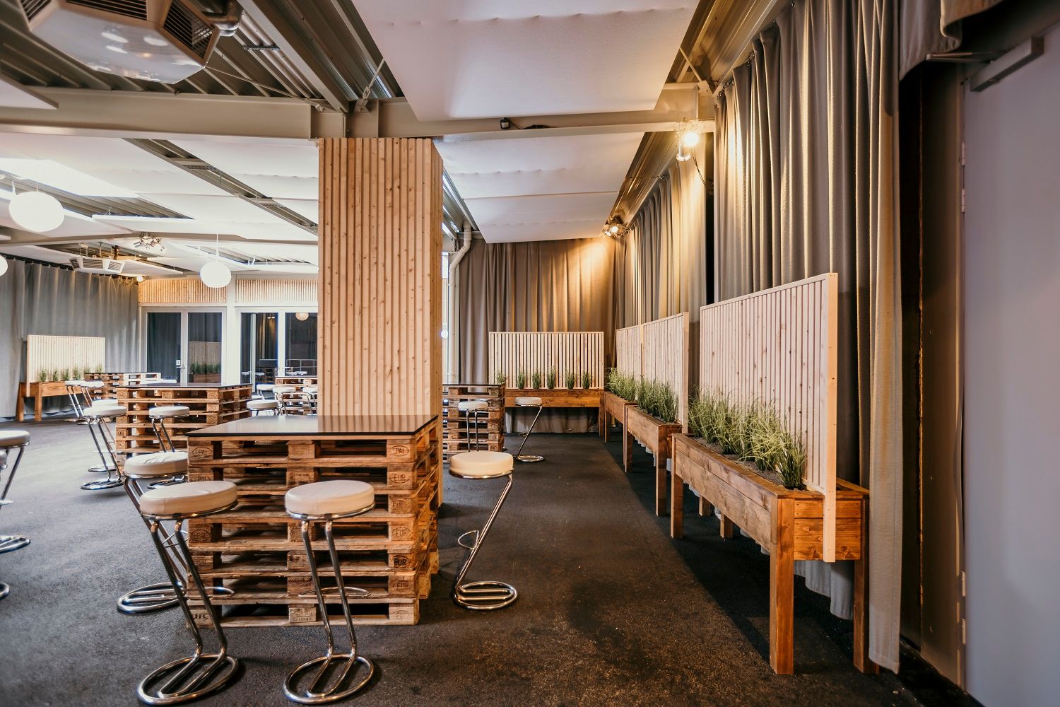 Interior view of the foyer of the ARENA NOVA congress hall with modern furniture made from pallets and plants.