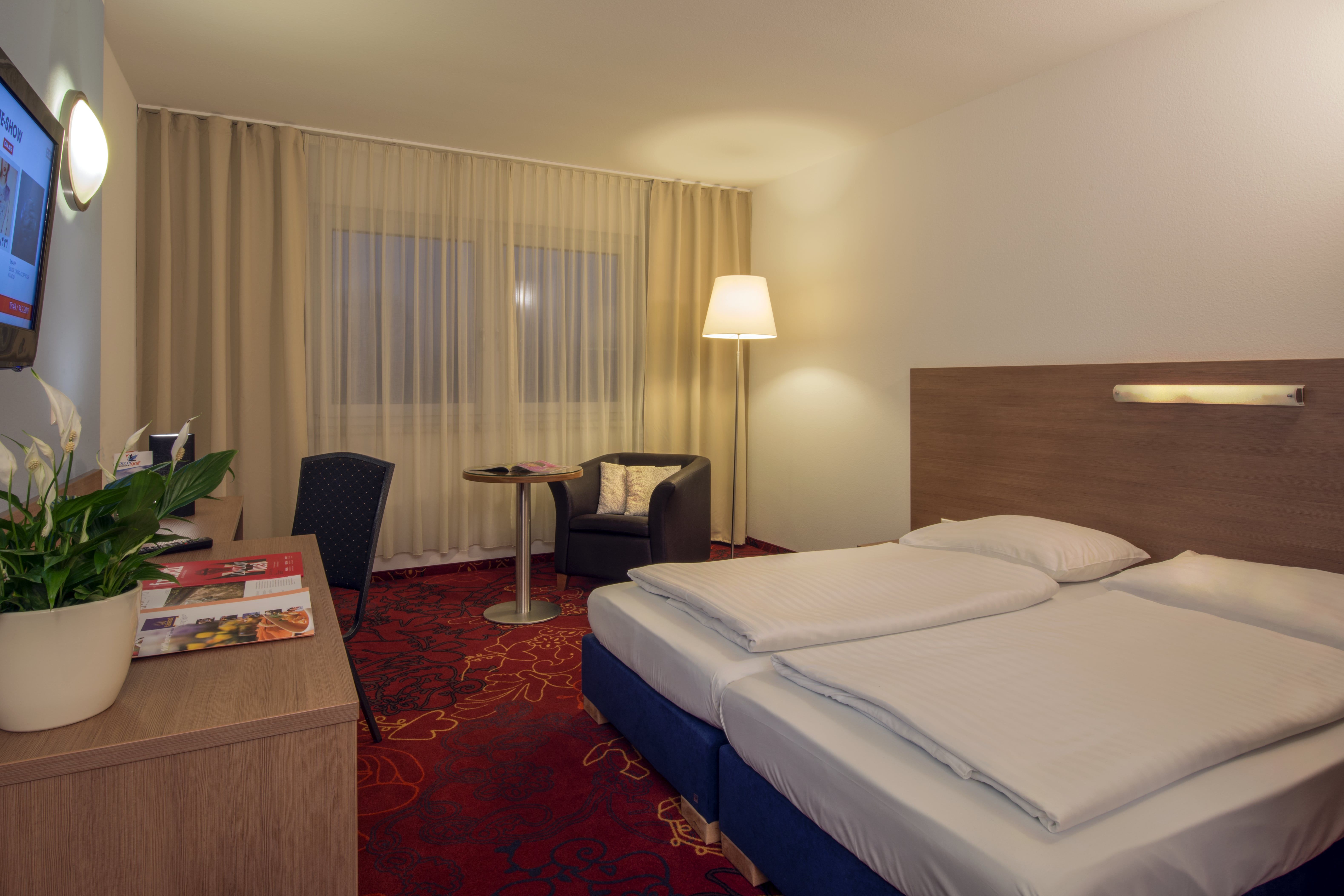 Double room with red carpeted floor, desk and large double bed.