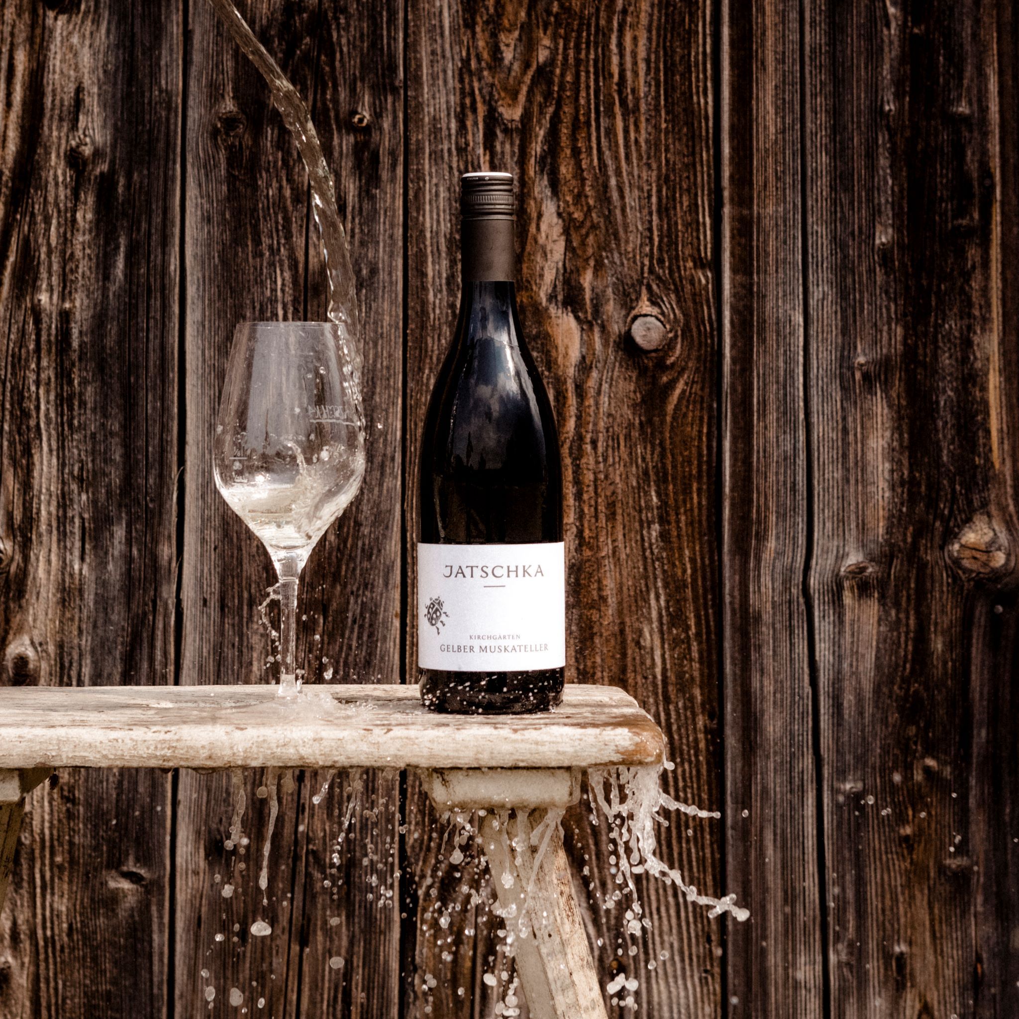 Wine bottle and glass with water in front of wooden wall.