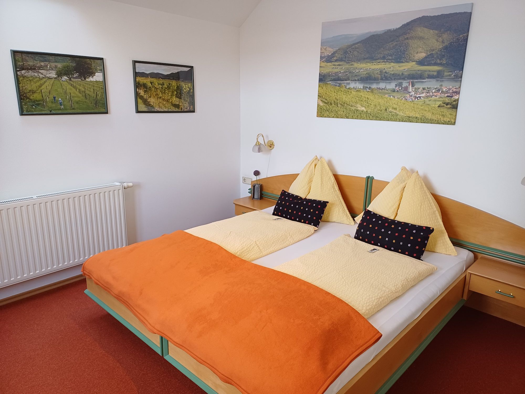 Cozy hotel room with double bed, orange ceiling and landscape pictures on the wall.