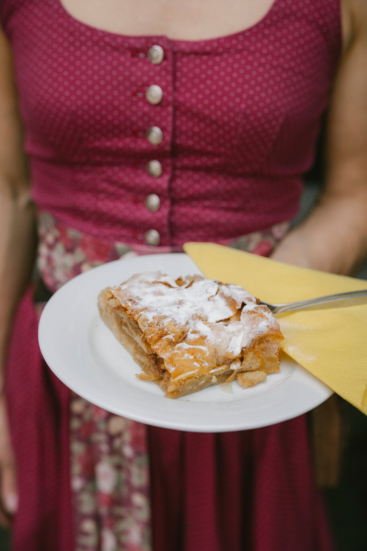 An employee wearing a dirndl presents a slice of apple strudel at the Hengsthütte on Schneeberg