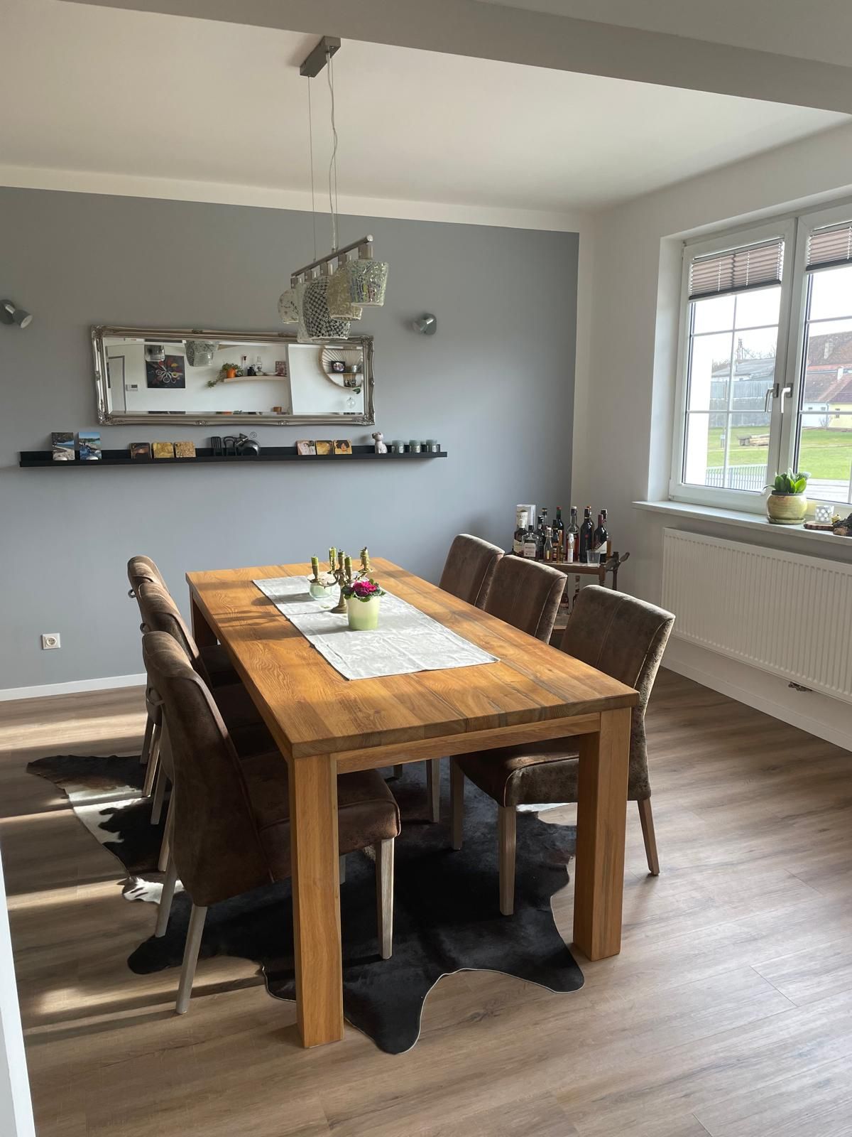Dining area with wooden table, six chairs, mirror and window.