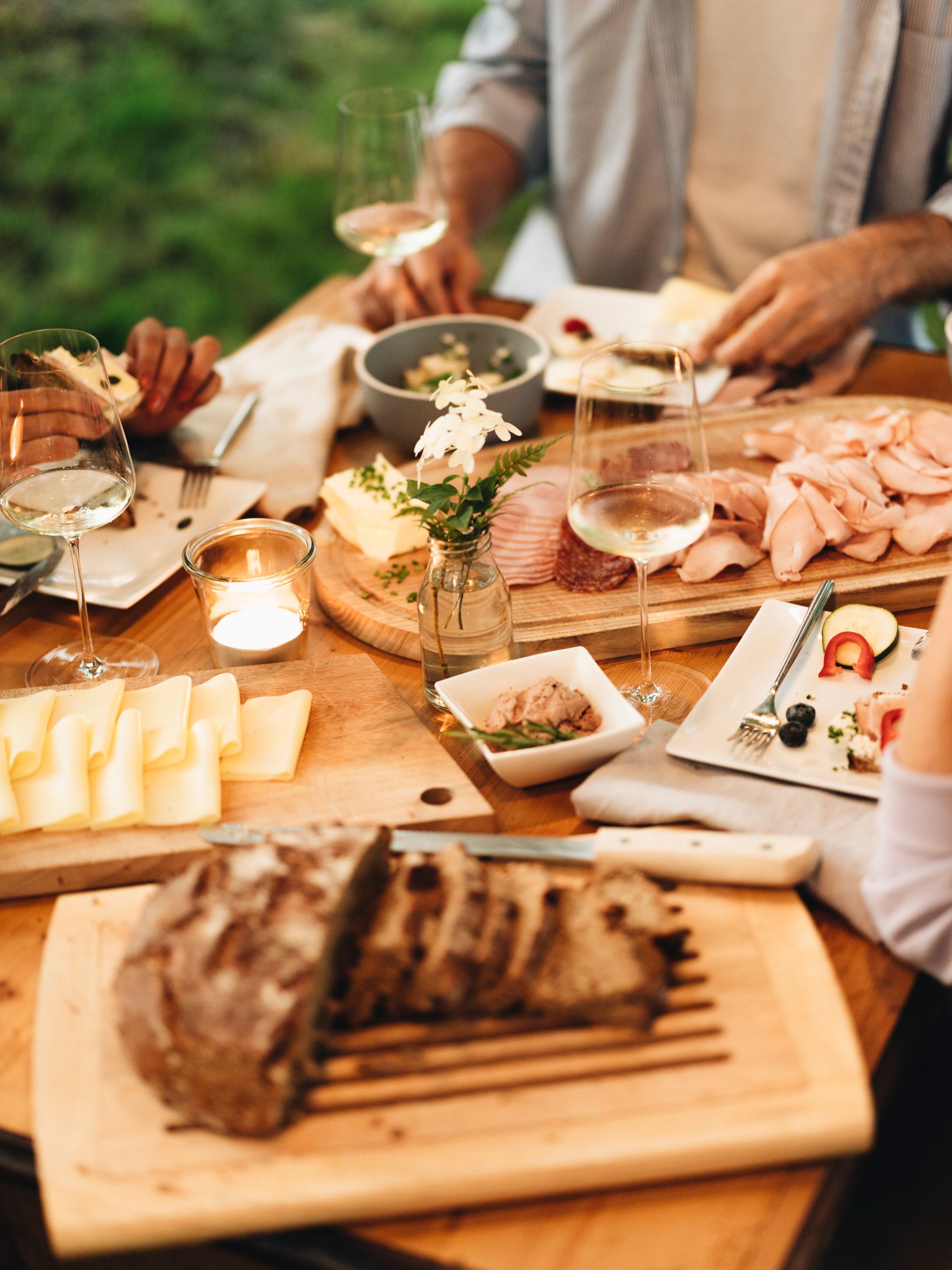 A table laid with bread, cheese, cold cuts and glasses of wine outside.