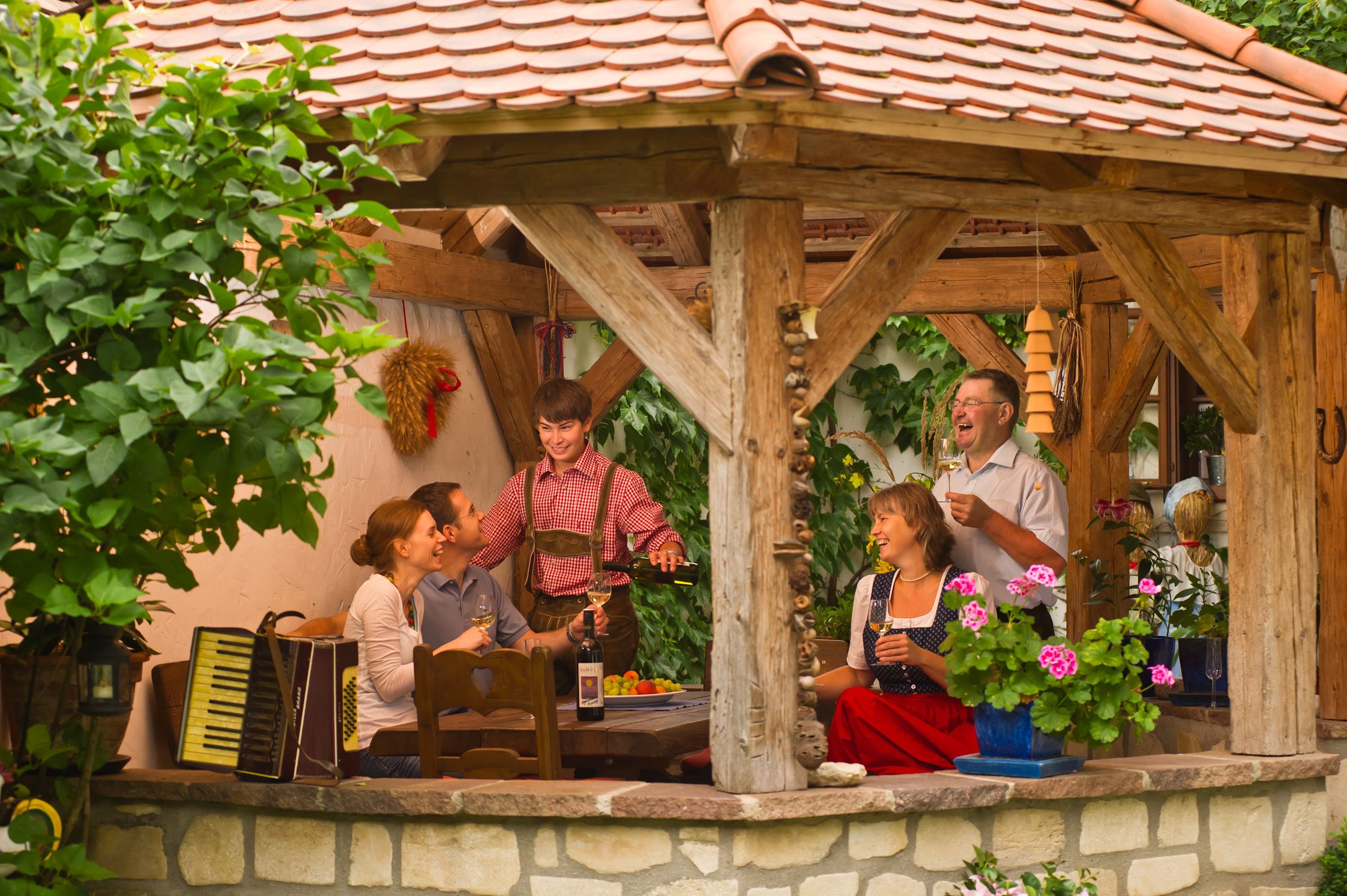 A group of people sit in a covered, rustic pavilion and enjoy wine and company.