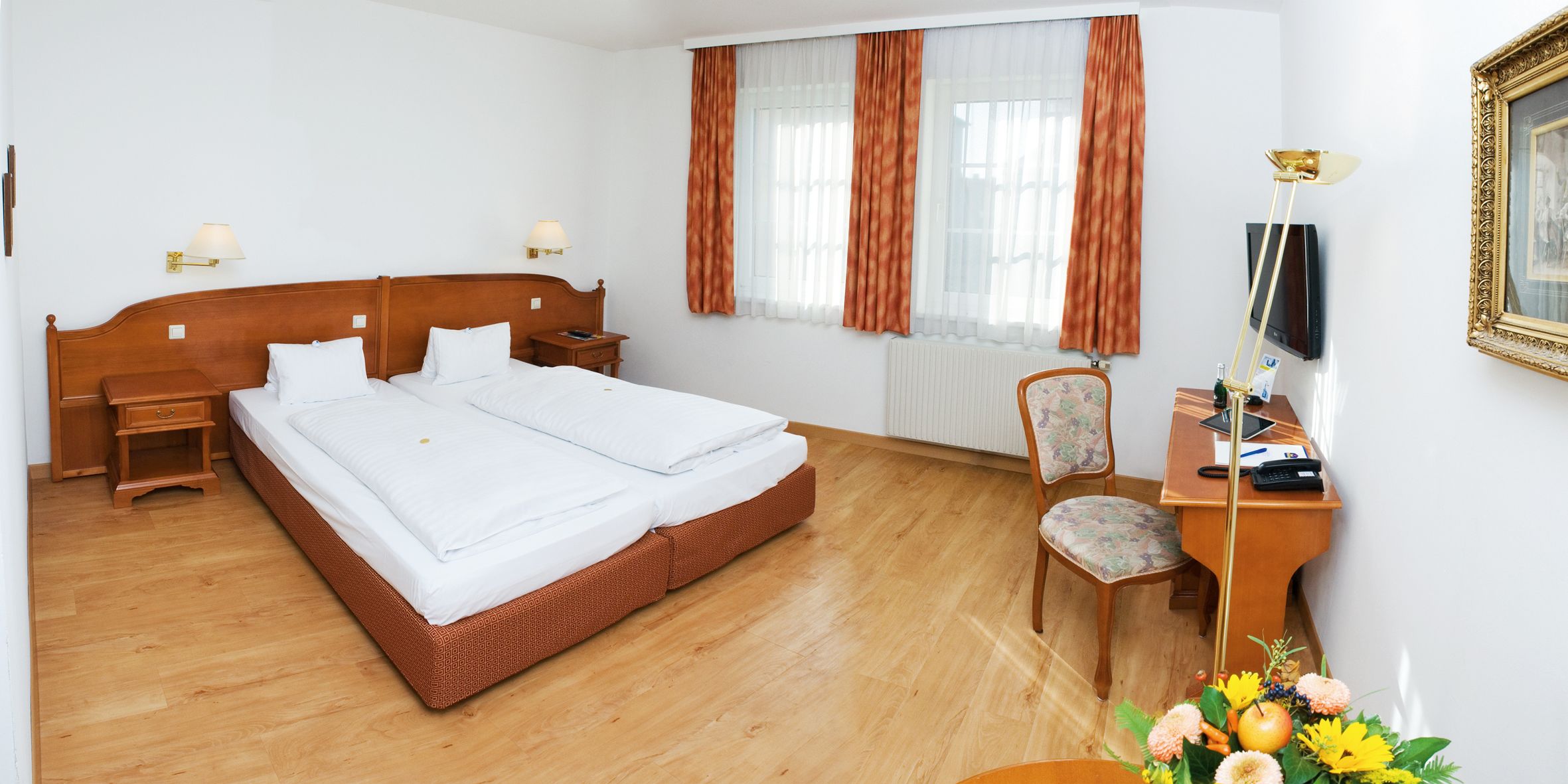 A cozy double room with two beds, wooden furniture and a desk with chair.