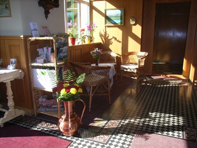 Entrance hall of a guesthouse with wicker furniture, flowers and decorative floor pattern.
