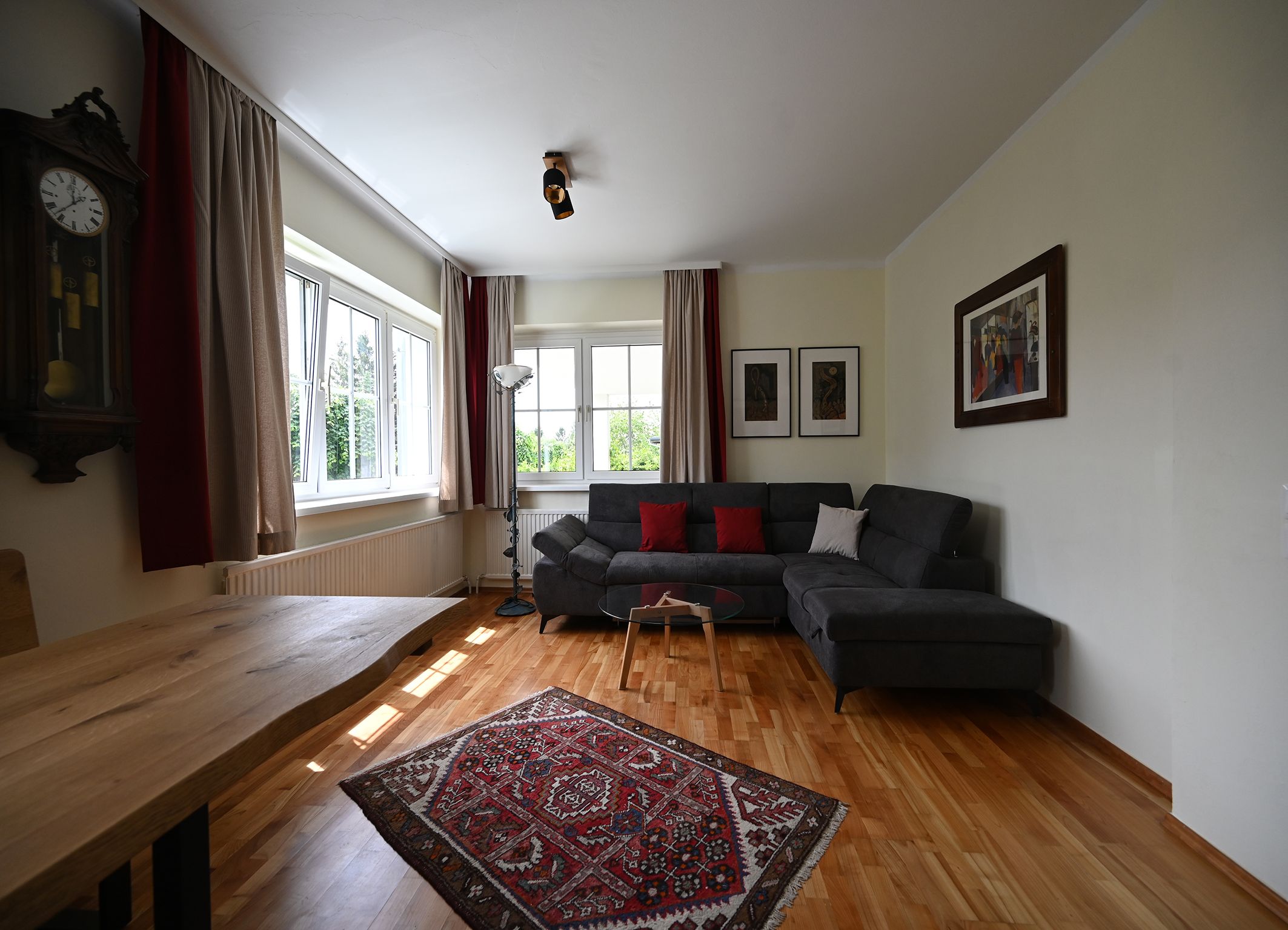 Modern living room with gray sofa, wooden table, carpet and wall clocks.