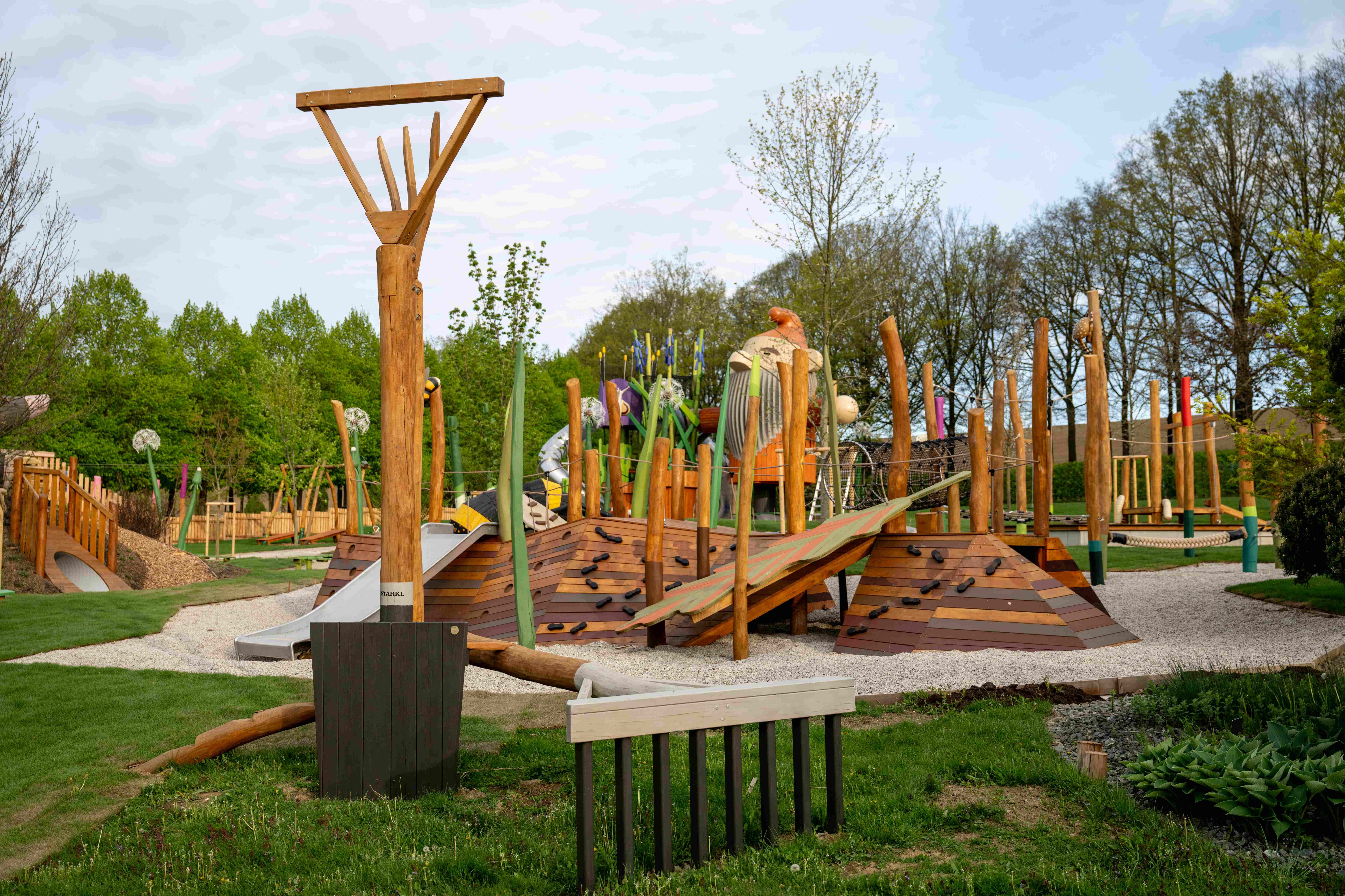A modern playground with wooden structures and climbing elements in a green park.