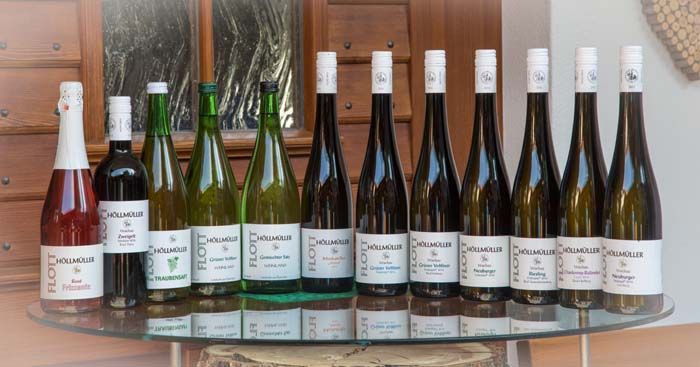 A selection of wine bottles on a glass table in front of a wooden wall.