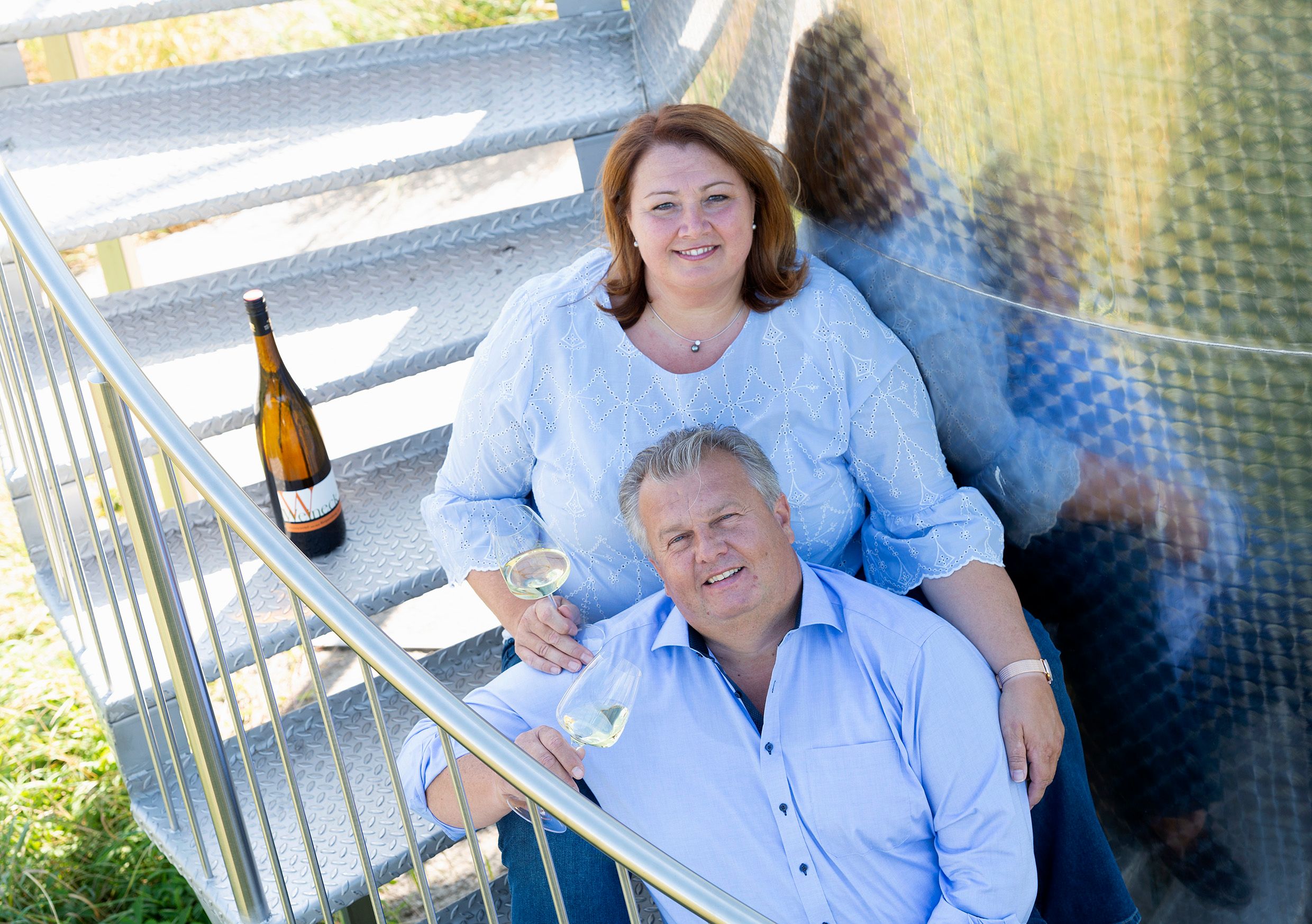 A man and a woman are sitting on a metal staircase with wine glasses in their hands.
