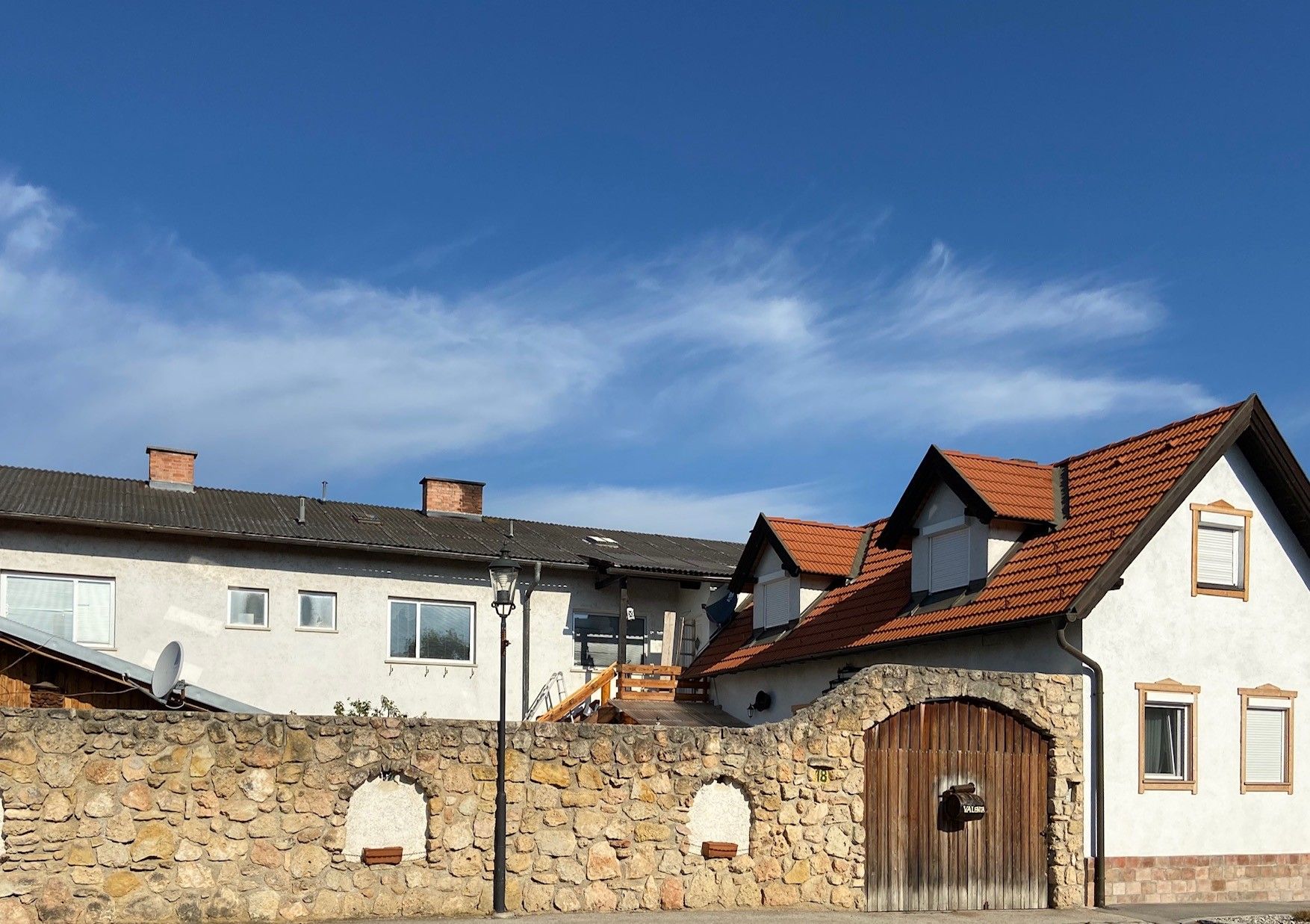 A building with red tiled roofs and a stone wall in the foreground under a blue sky.