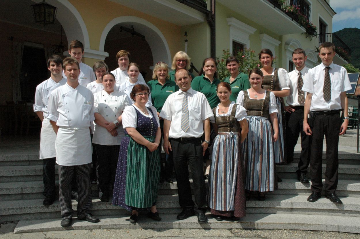 A group of people in work clothes stand in front of a building with arches.