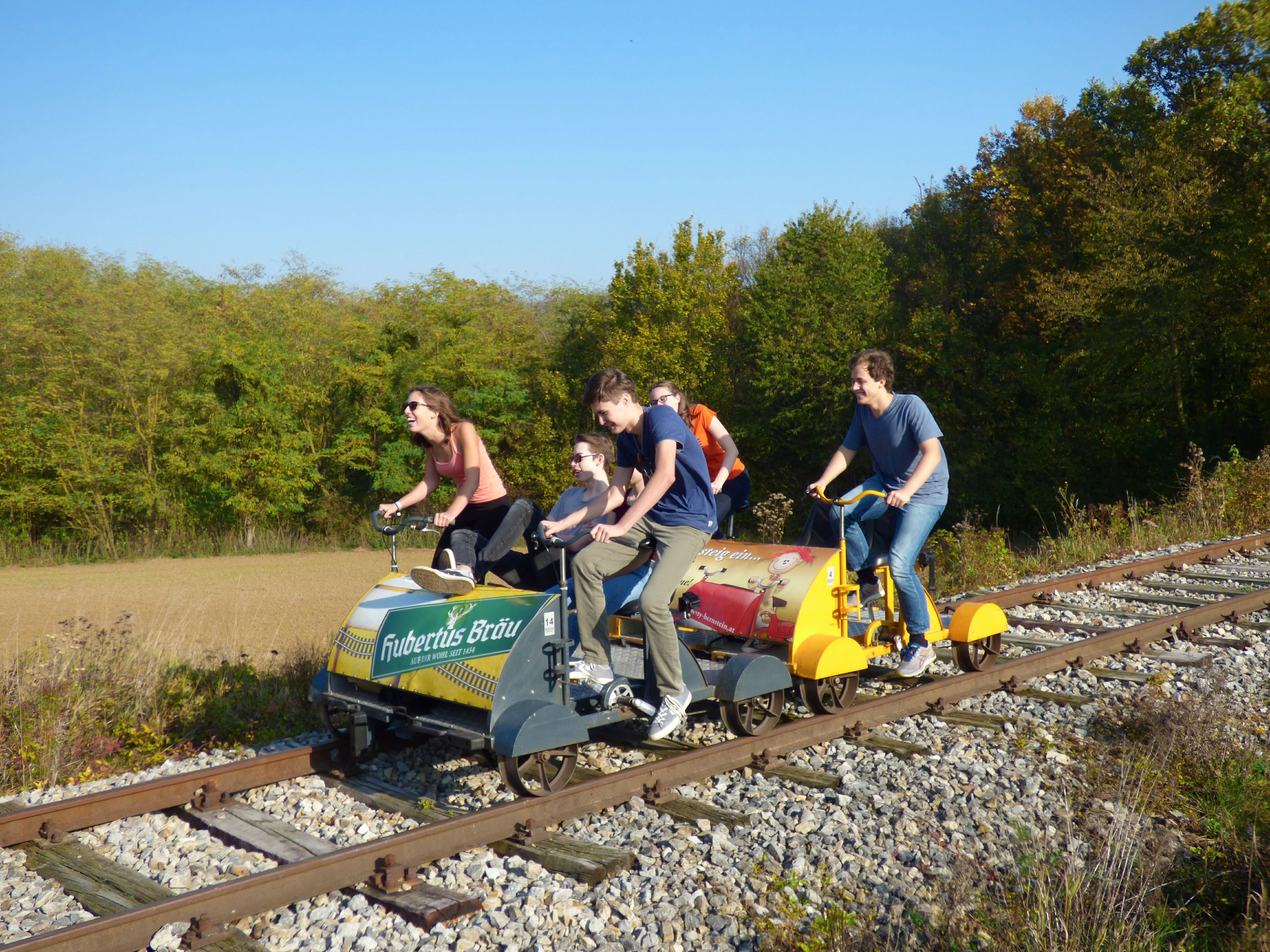 Group of people riding a trolley on railroad tracks through a rural landscape.