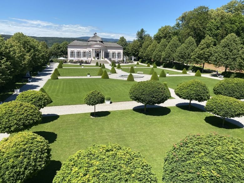Baroque park with symmetrical paths, manicured lawns and a pavilion in the background.