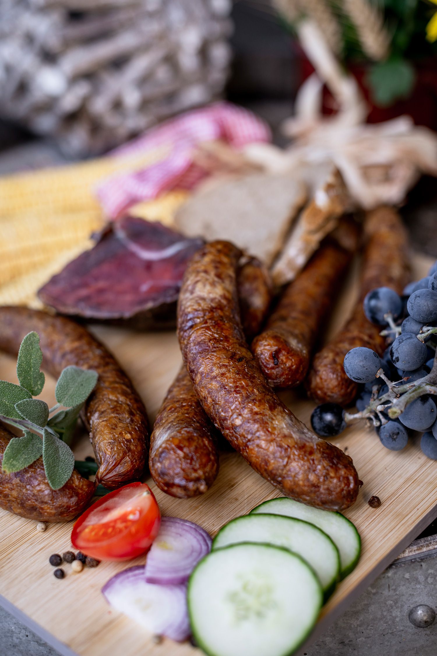 Close-up of sausages, grapes, tomatoes, cucumbers and onions on a wooden board.