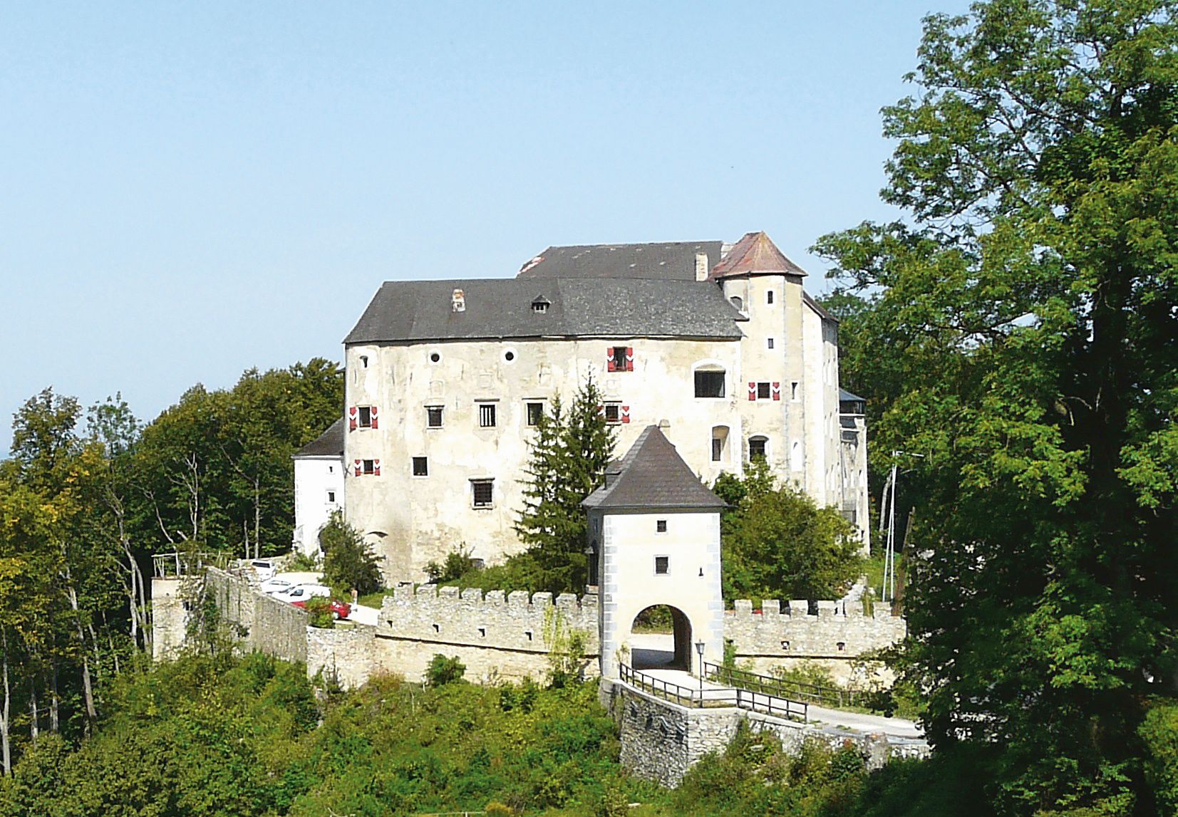 Historic castle with a white façade and battlements, surrounded by trees.