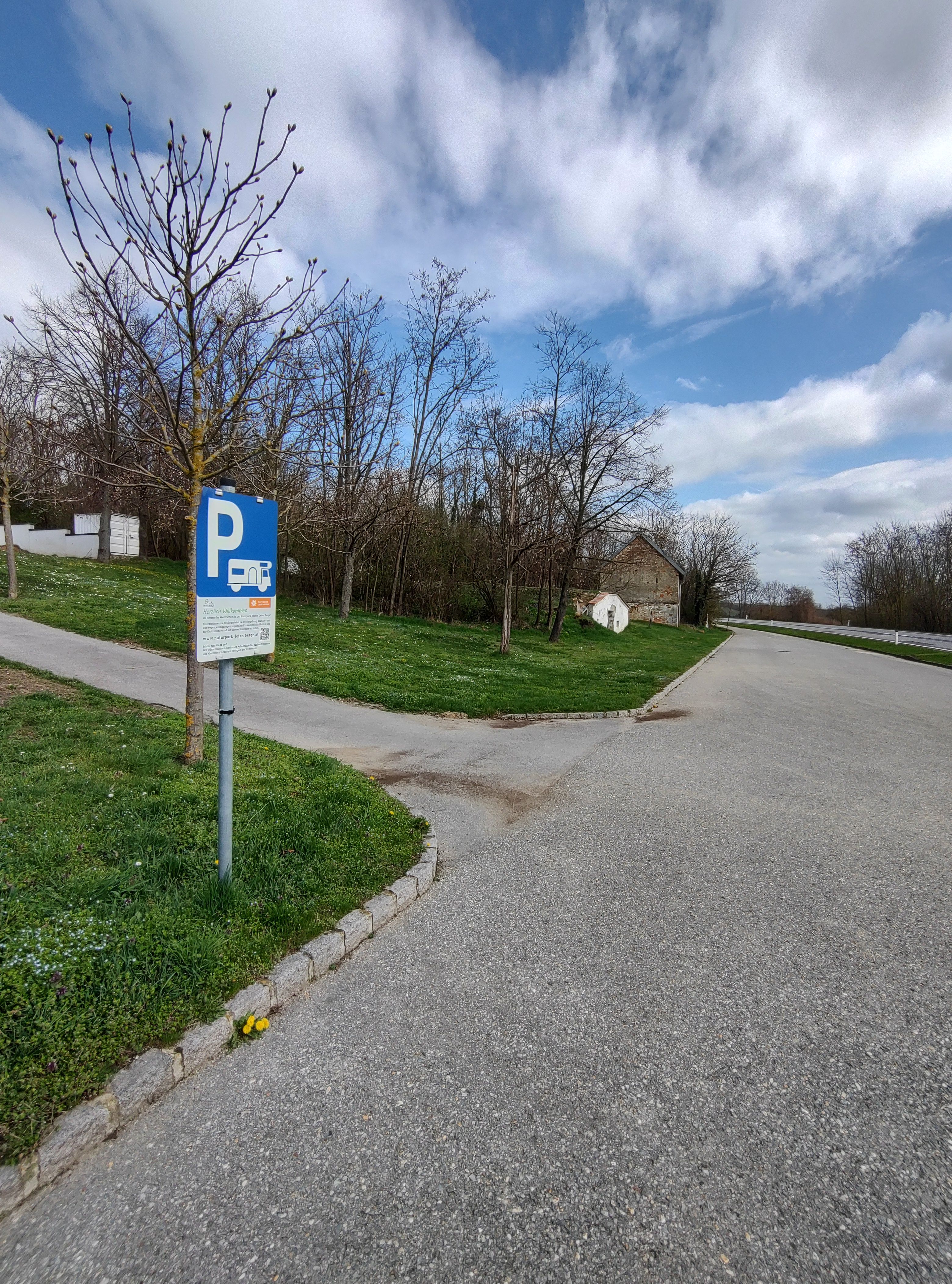 Motorhome parking space with parking lot sign and trees in the background.