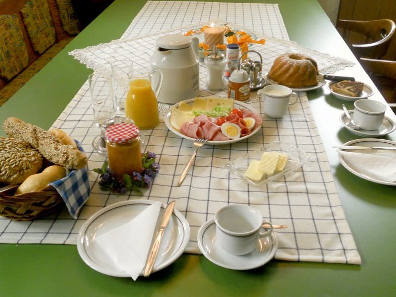 A laid breakfast table with bread rolls, cold cuts, cheese, juice, coffee and cake.