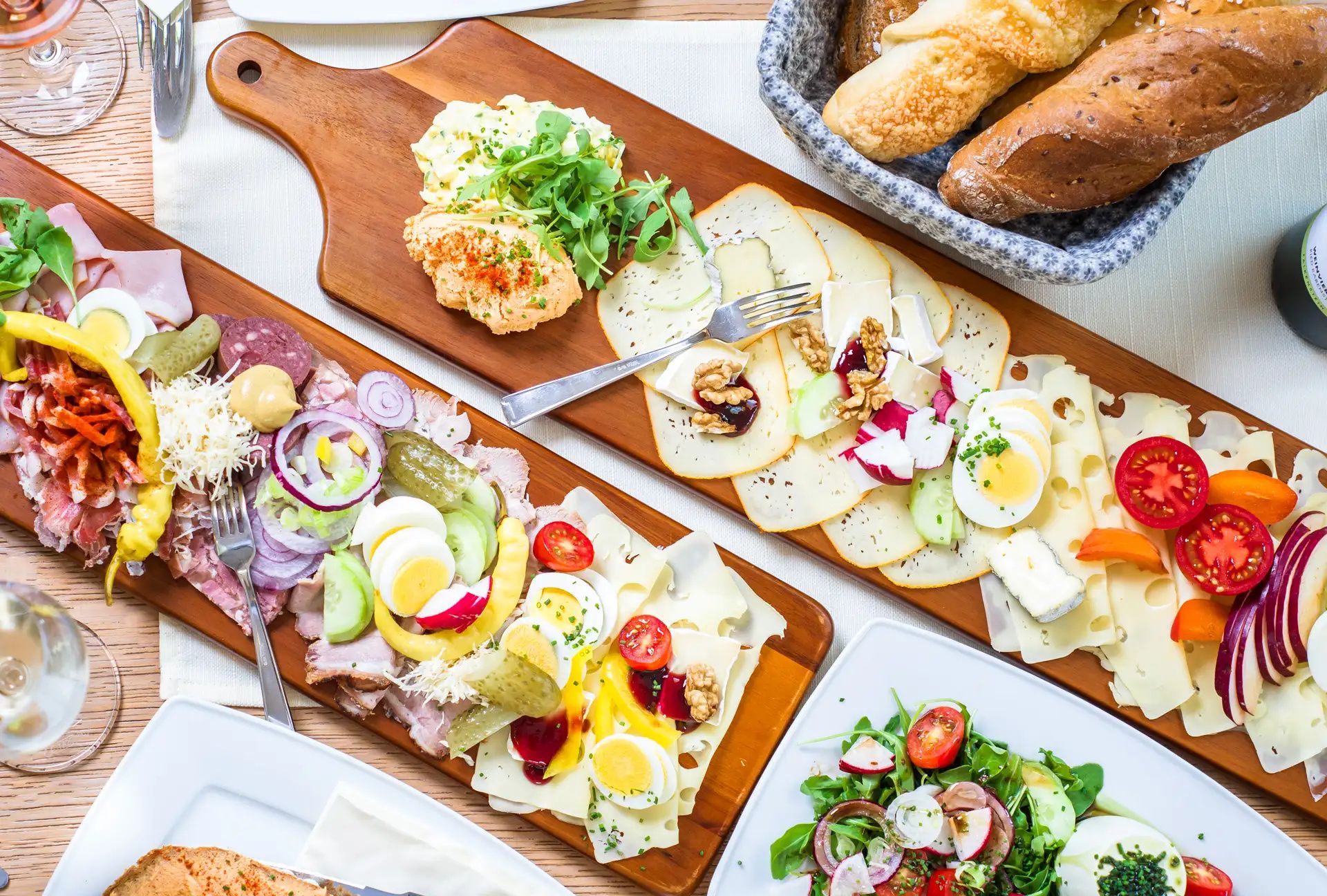 Various cold cuts and cheese platters with bread and salad on a table.