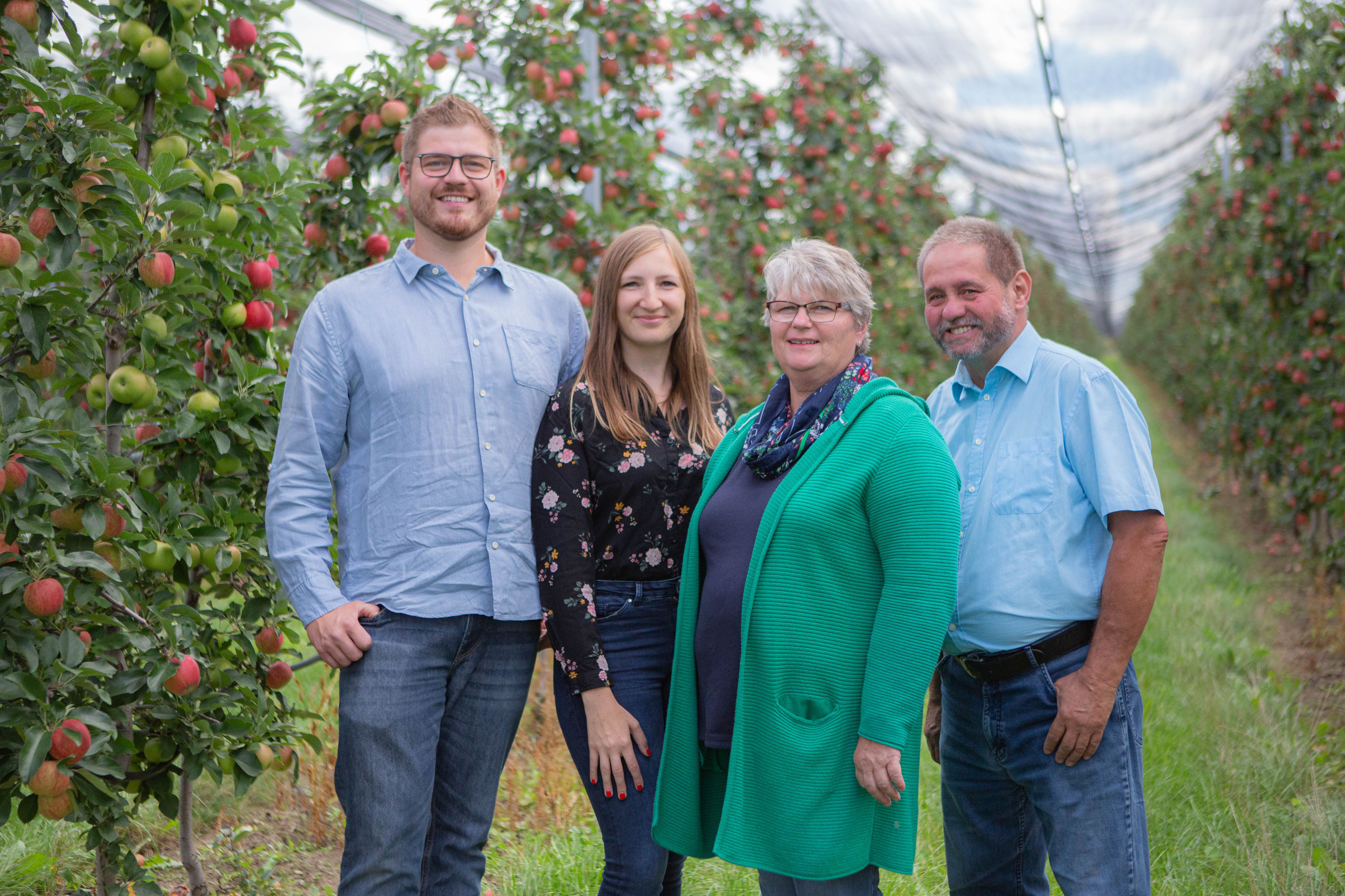 Four people are standing in an apple orchard.