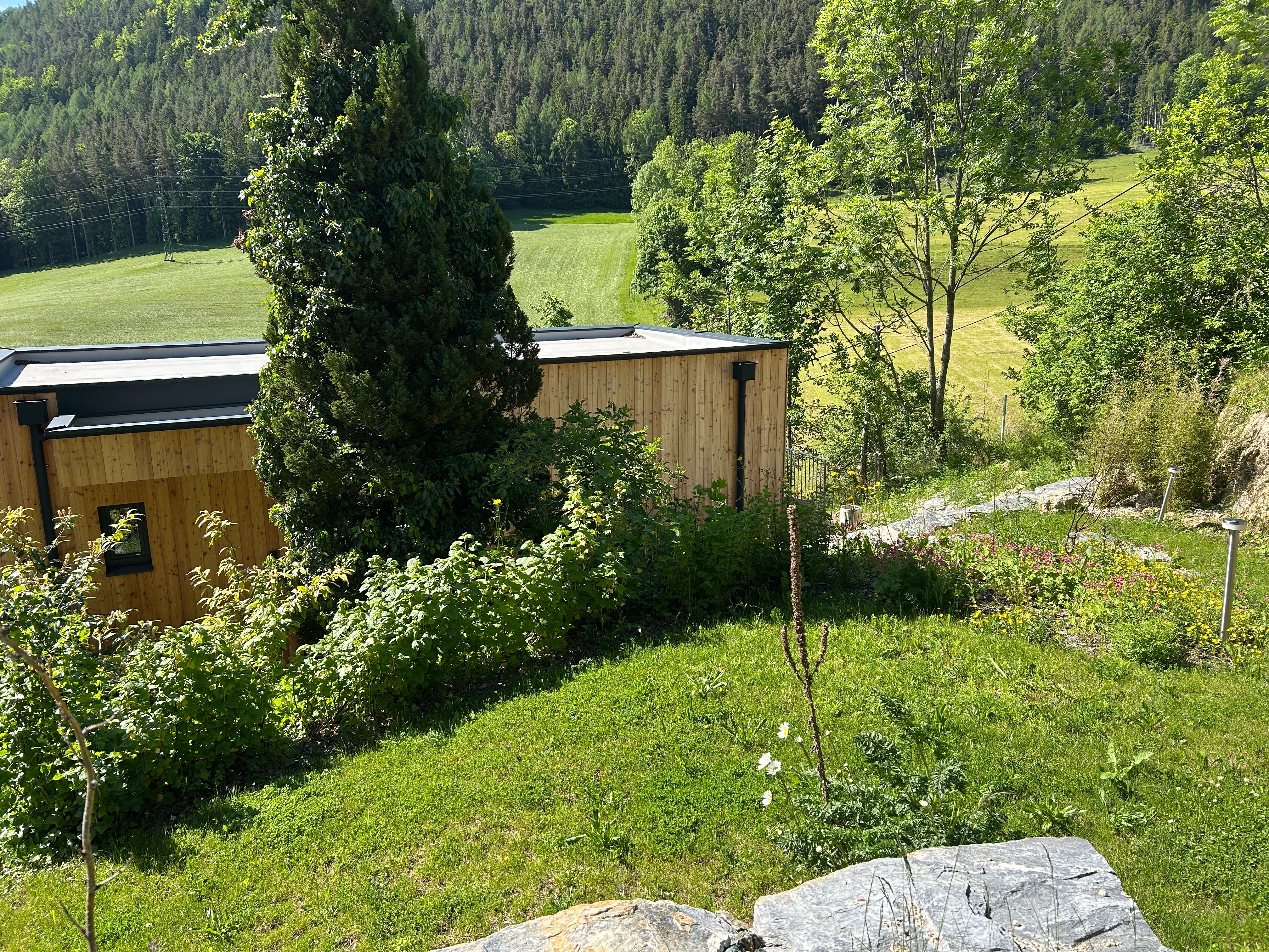 A modern wooden house in a green, hilly landscape with trees and meadows.
