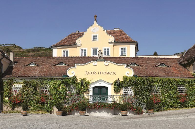 Historic building with the inscription 'Lenz Moser', surrounded by plants and flowers.