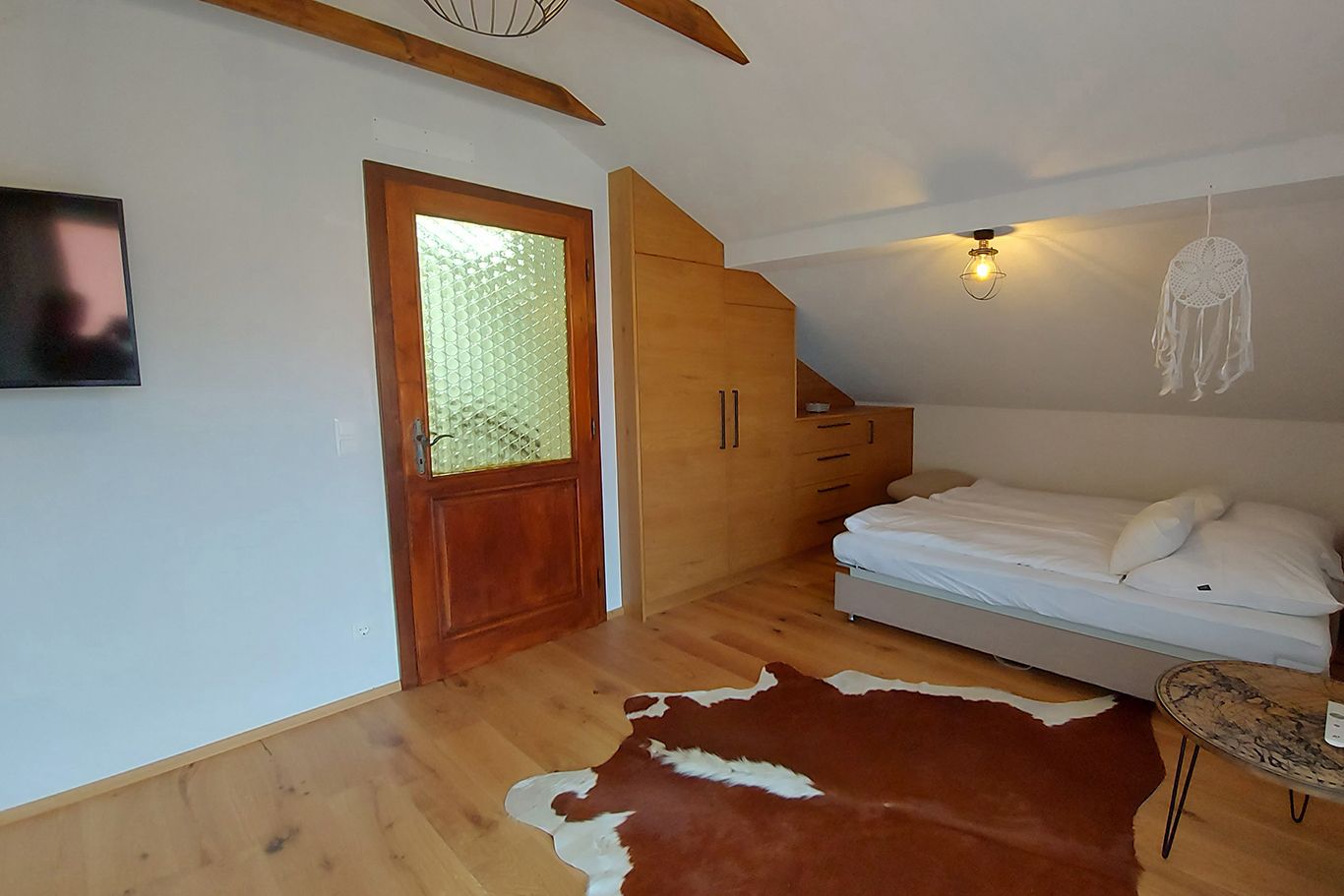 Bedroom with wooden floor, bed, wardrobe, door and TV.