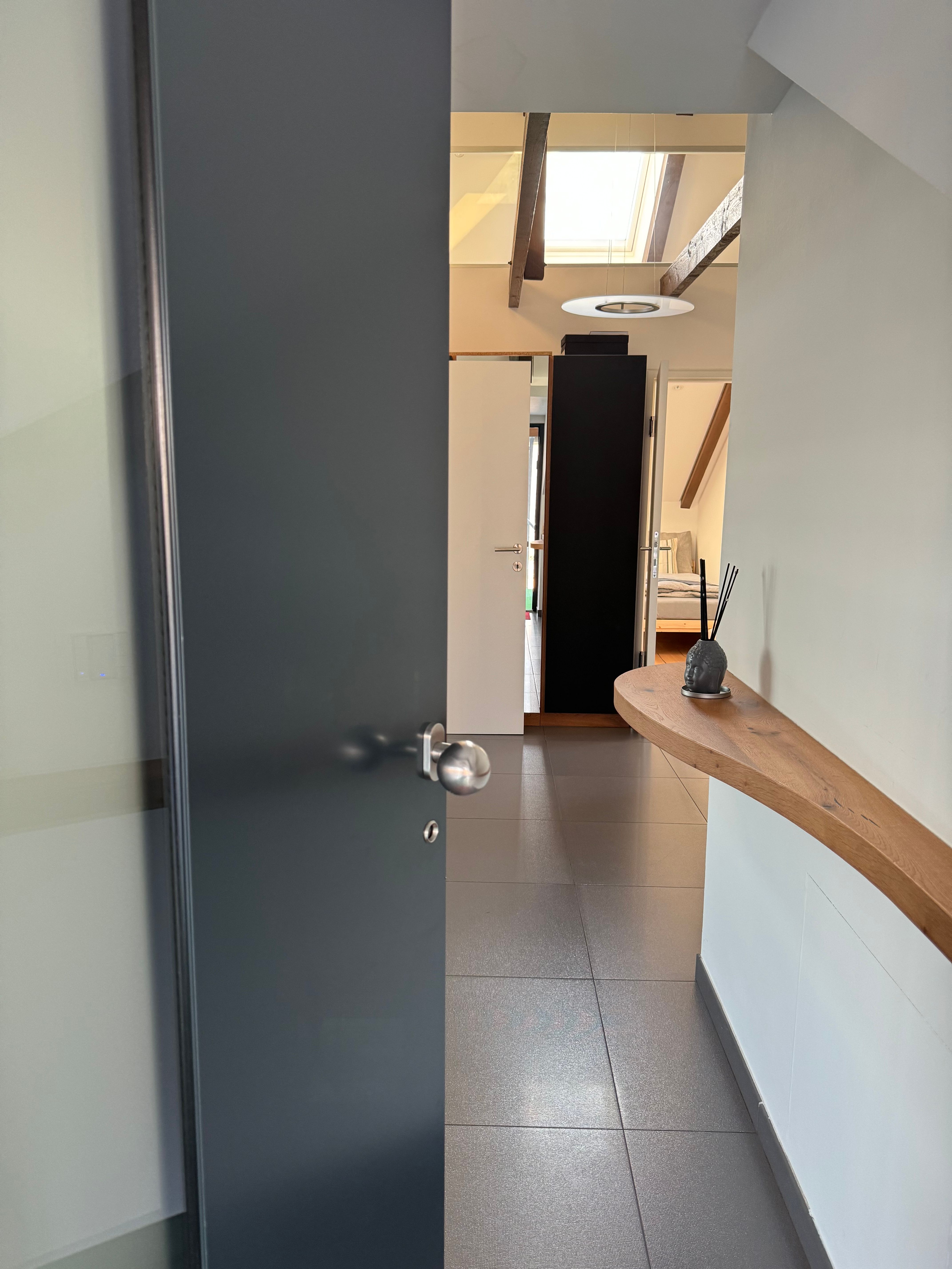 Modern entrance area with open door, tiled floor and wooden shelf on the wall.