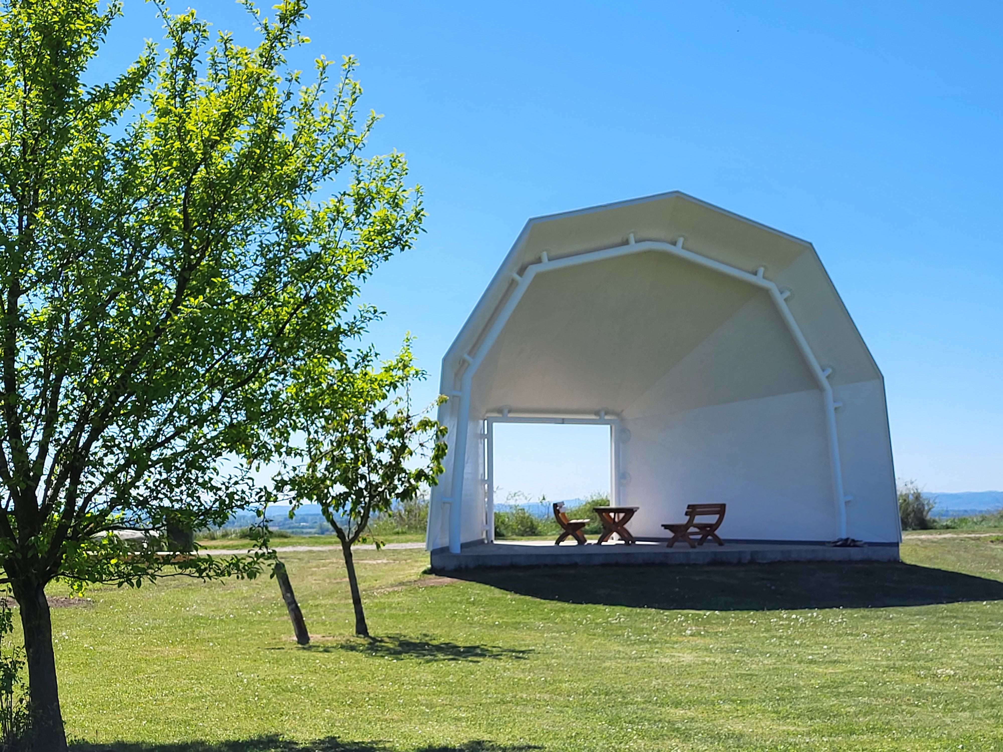 Covered rest area with seating on a meadow under a blue sky.
