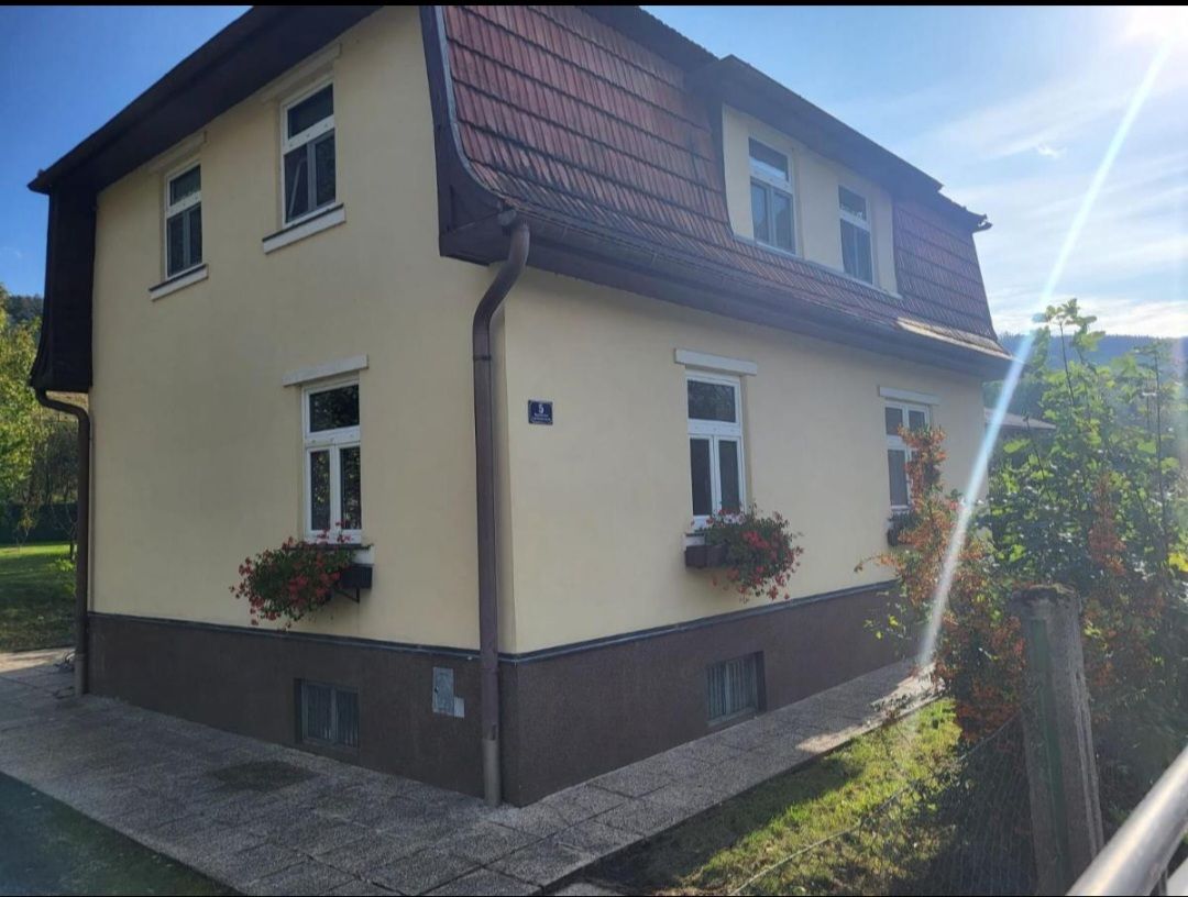 Two-storey yellow house with red roof tiles and flower boxes on the windows.