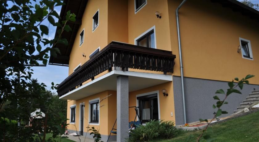 Yellow house with balcony and garden, surrounded by plants.