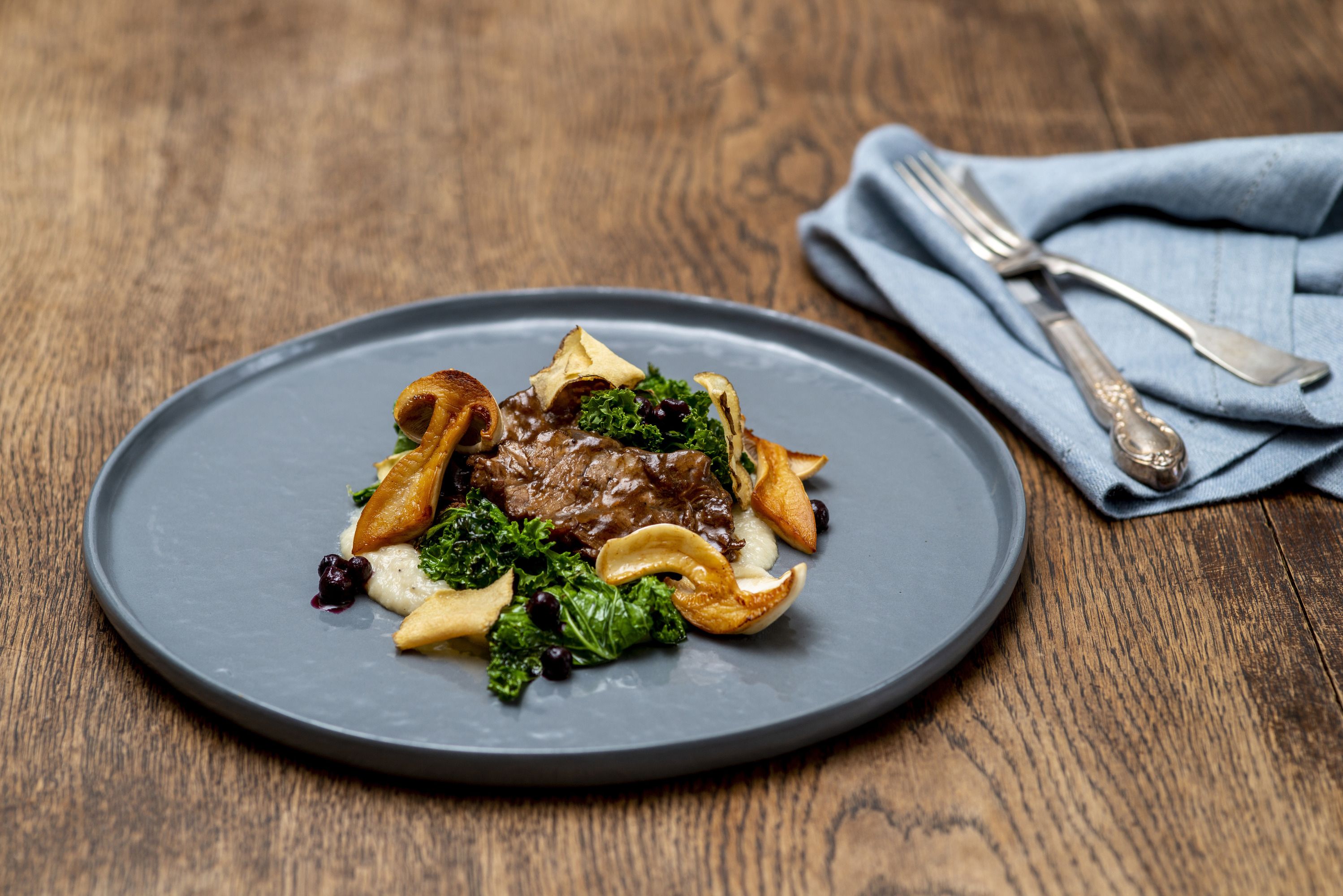 Gourmet dish with meat, mushrooms and kale on a gray plate.