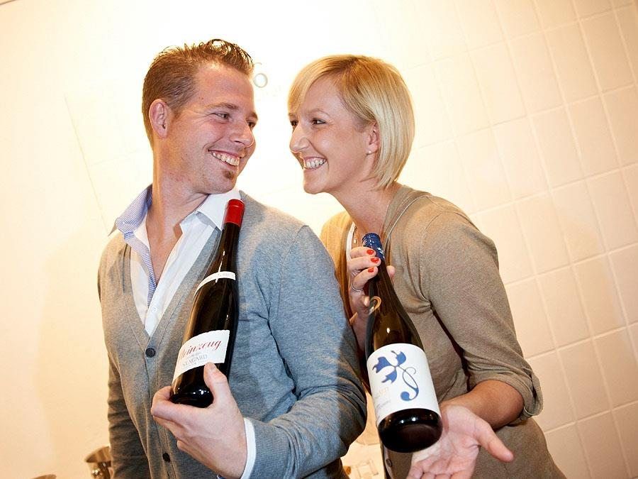 A man and a woman smile at each other and hold bottles of wine in their hands.