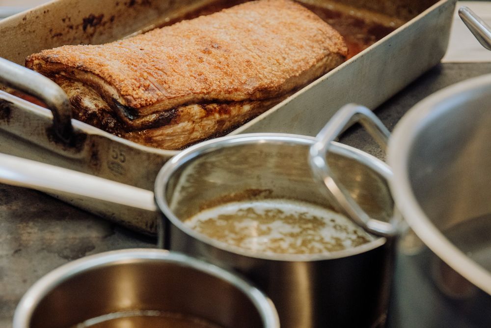 Crispy roast pork in a metal pan, pots of gravy next to it.
